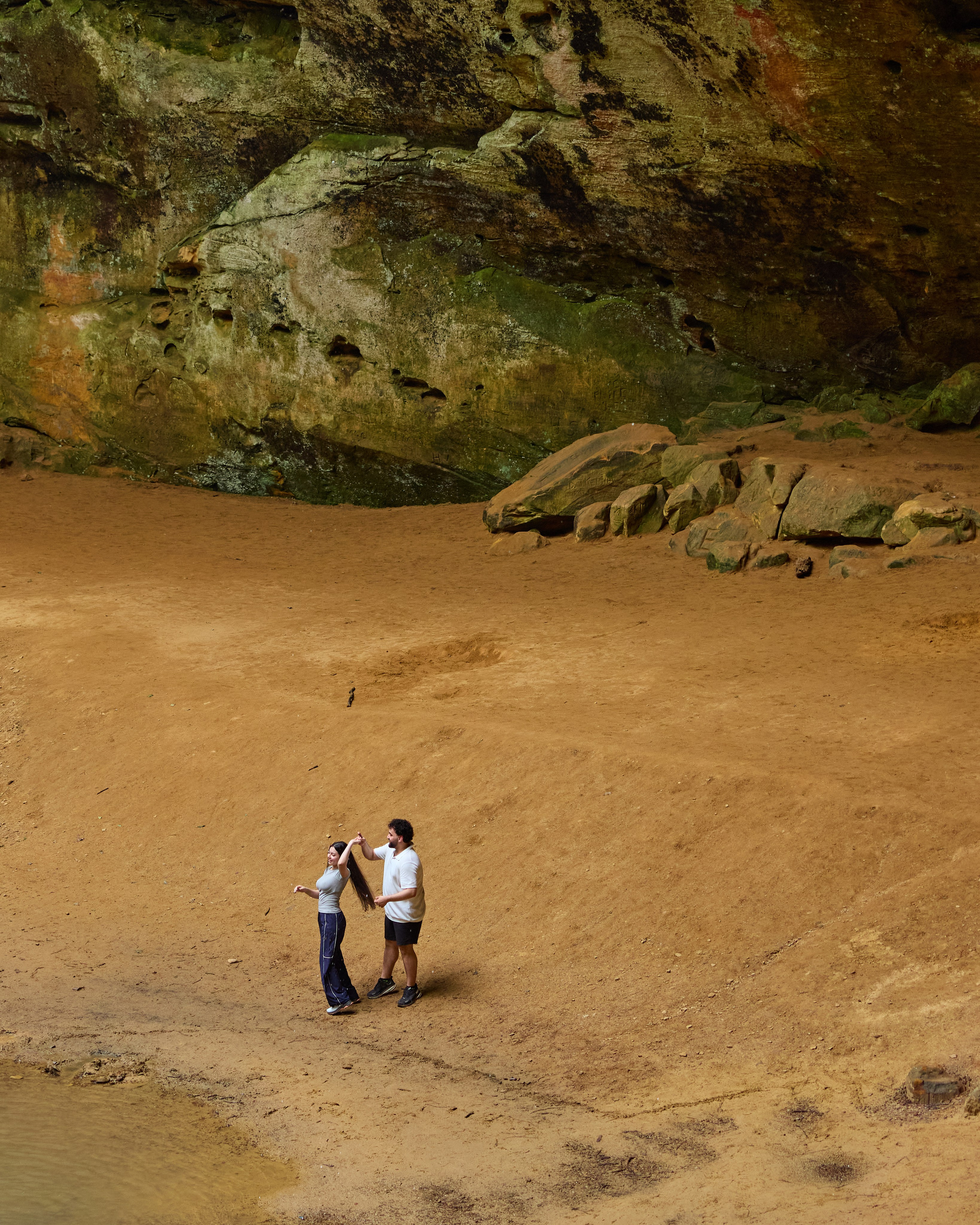 Wide view of a couple dwarfed by the sandstone gorge in Hocking Hills, Ohio