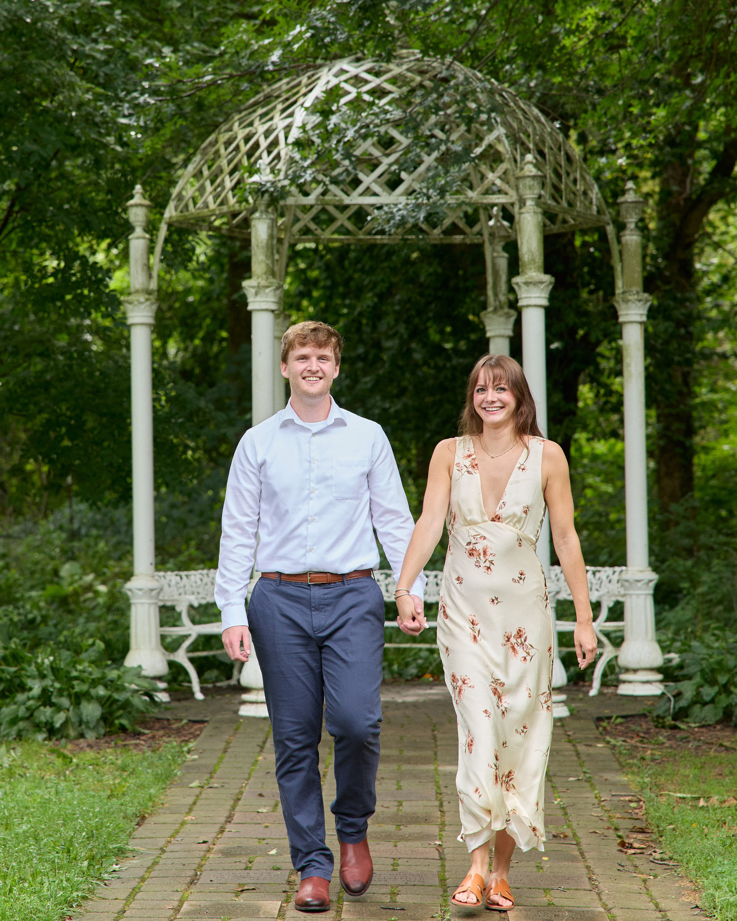 Newly engaged couple walking hand in hand toward the camera at the Park of Roses in Columbus, Ohio