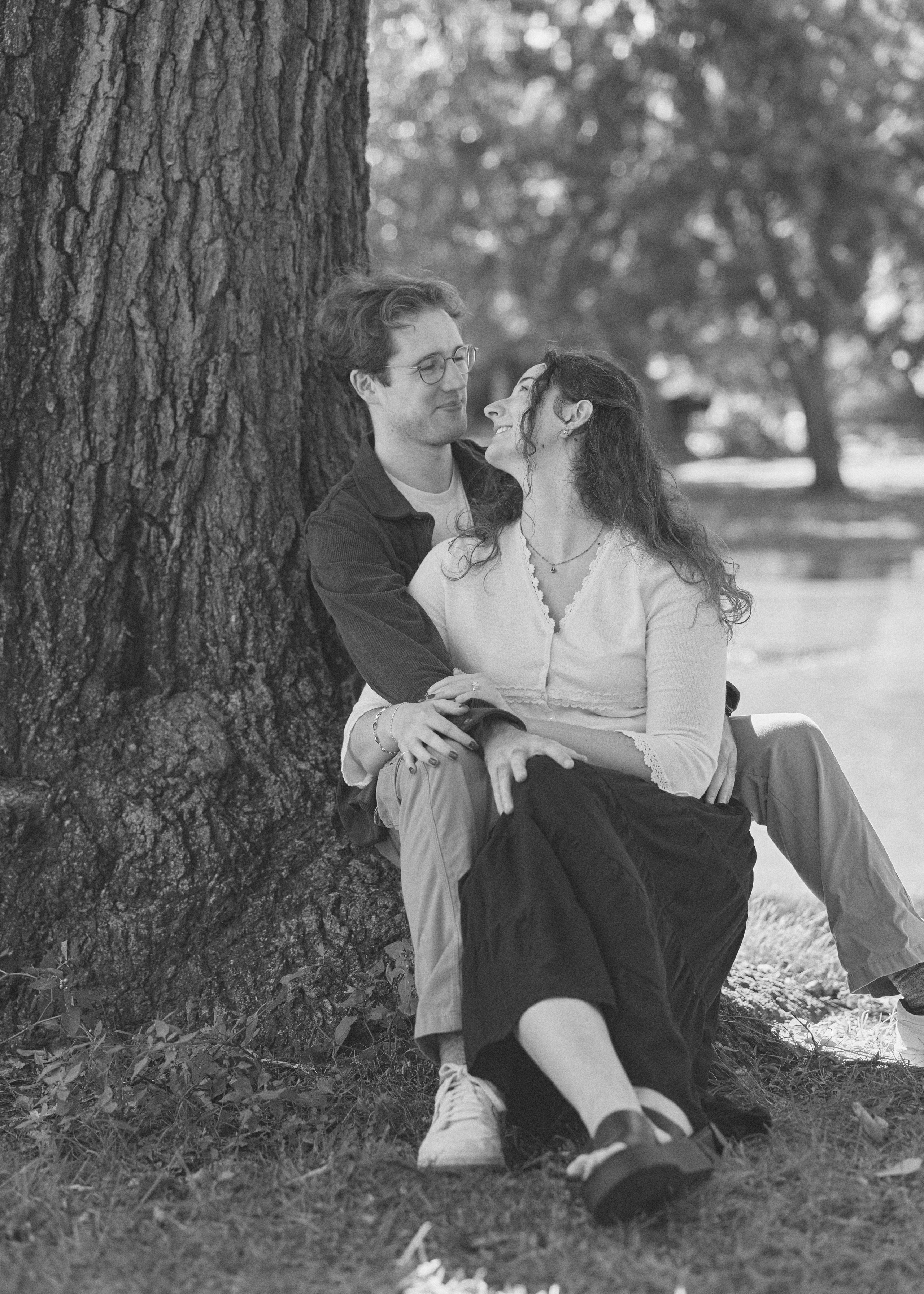 Black and white photo of a couple sitting together against a tree trunk in Columbus, Ohio