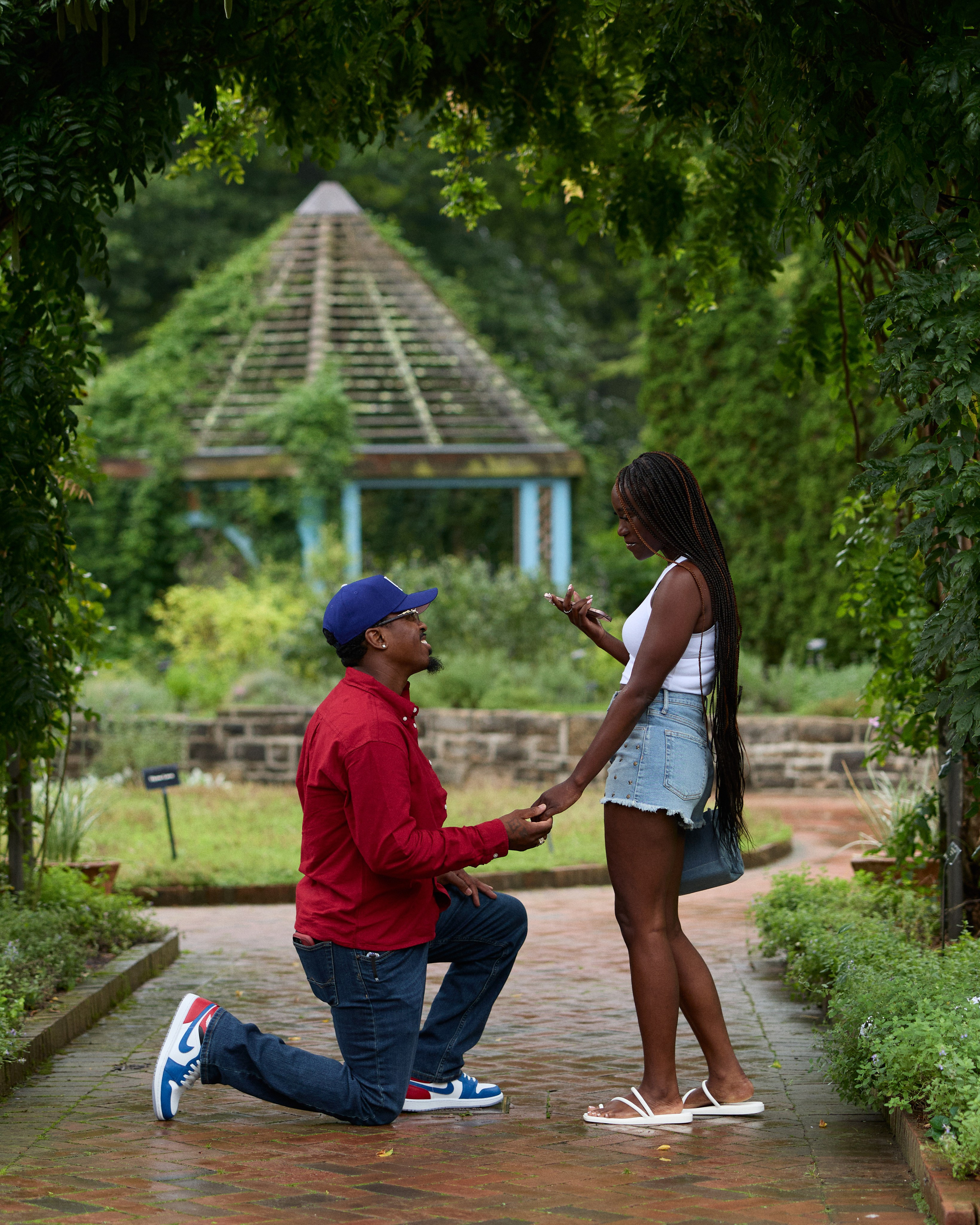 Man in a red shirt proposing on a brick path near the gazebo at Inniswood Metro Gardens, Ohio