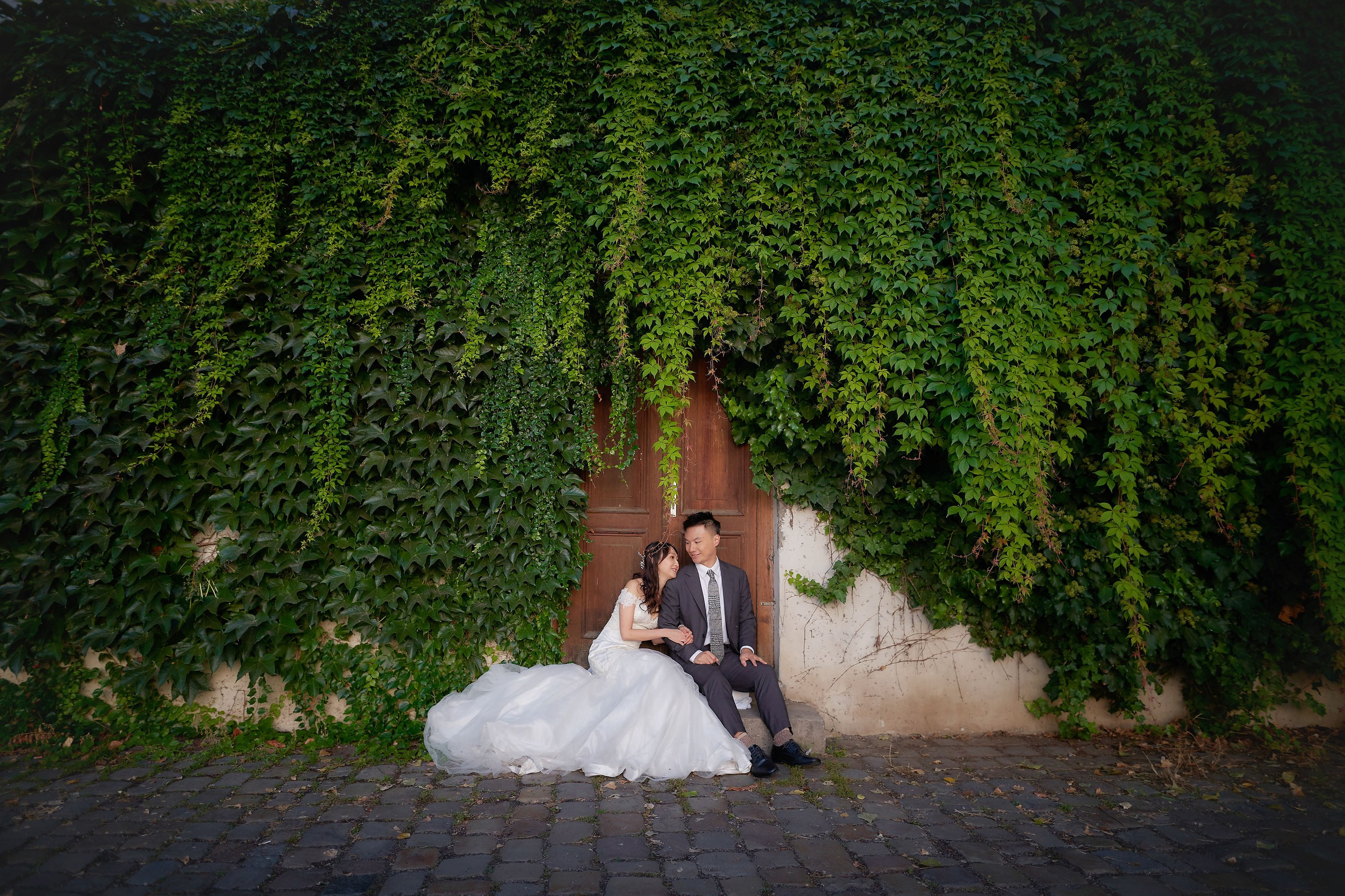 Newlyweds Eva and Conan are sitting under an ivy wall watching the sunrise over Charles Bridge.