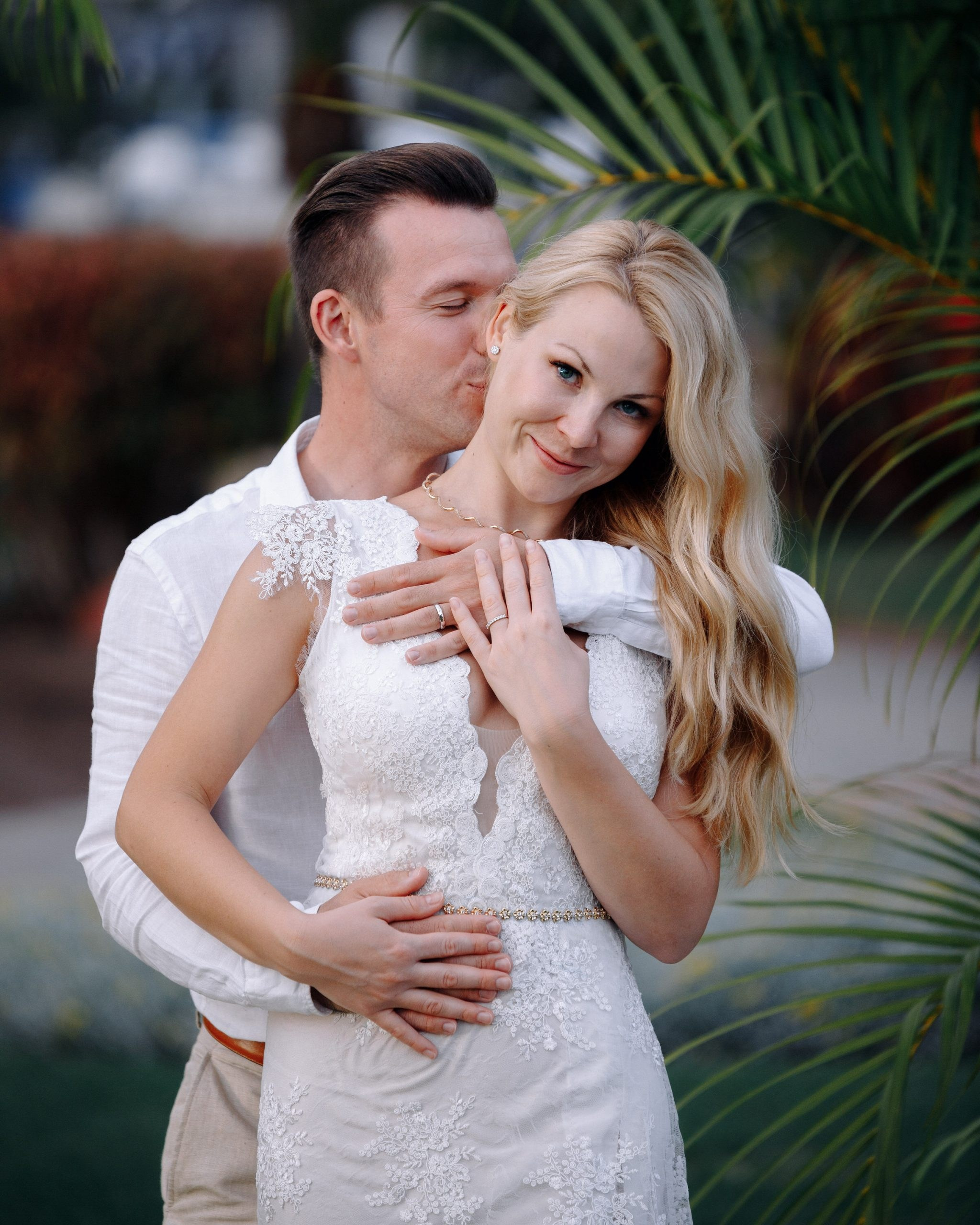 Une mariée et un marié s'embrassant devant des palmiers.
