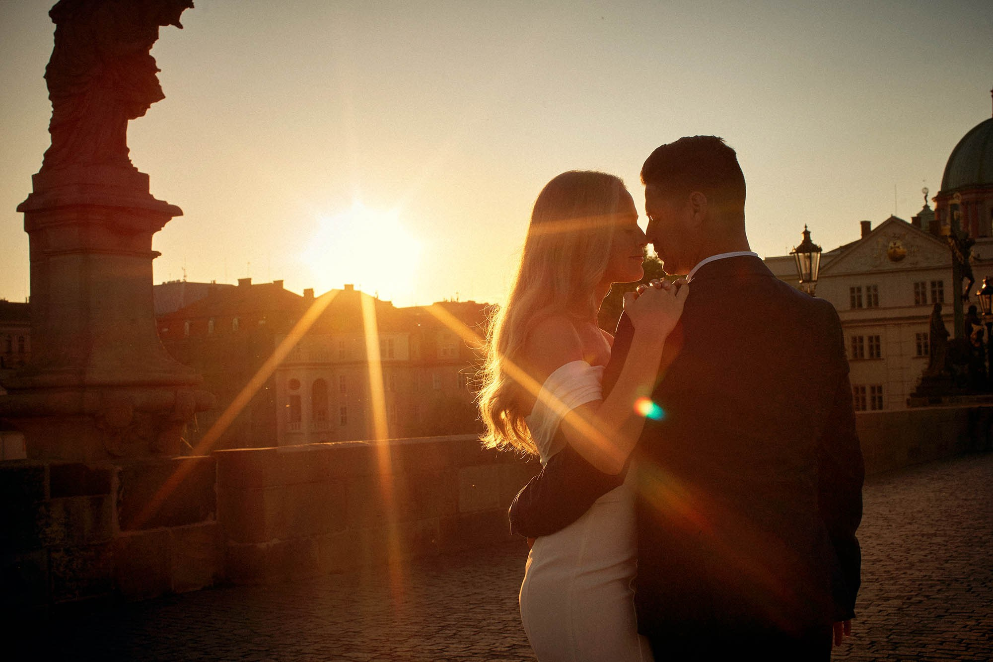 A couple embraces as lens flare surrounds them on the Charles Bridge in Prague