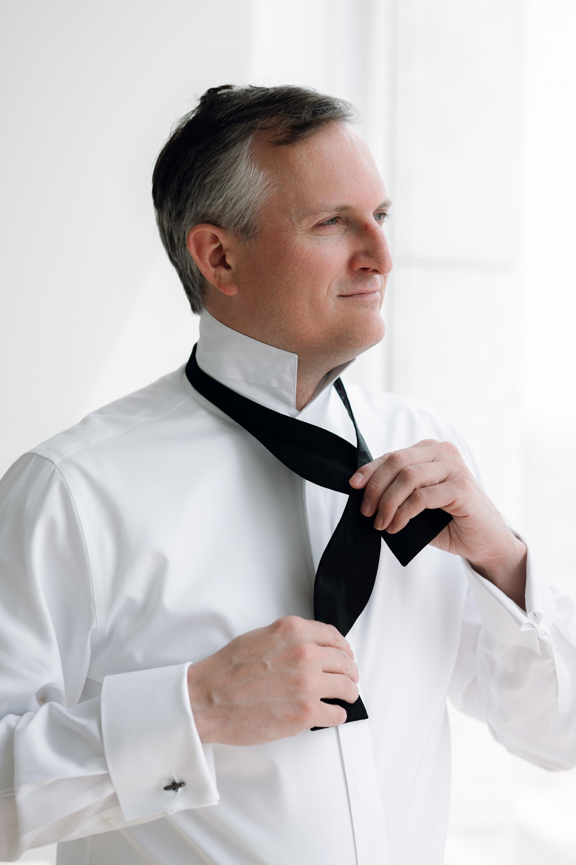 a man in a white shirt tying a black tie