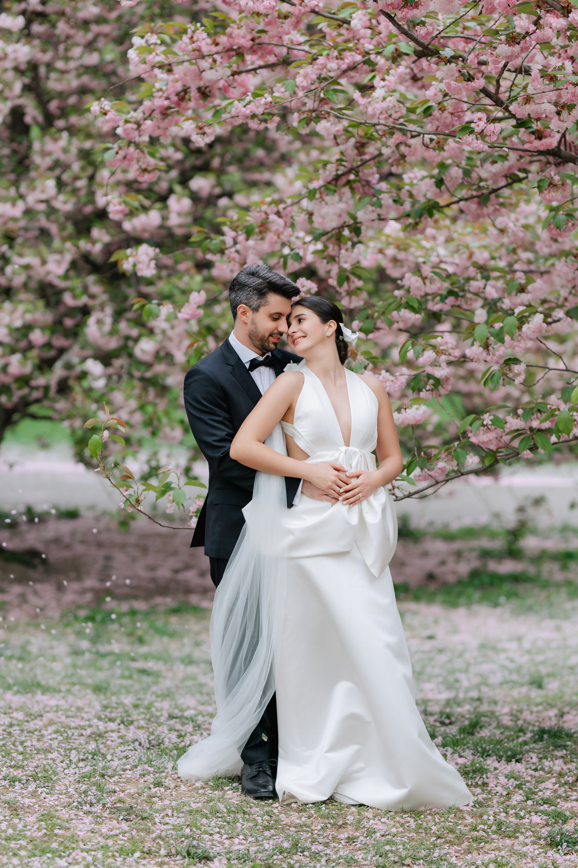 a bride and groom pose in front of a tree with pink flowers