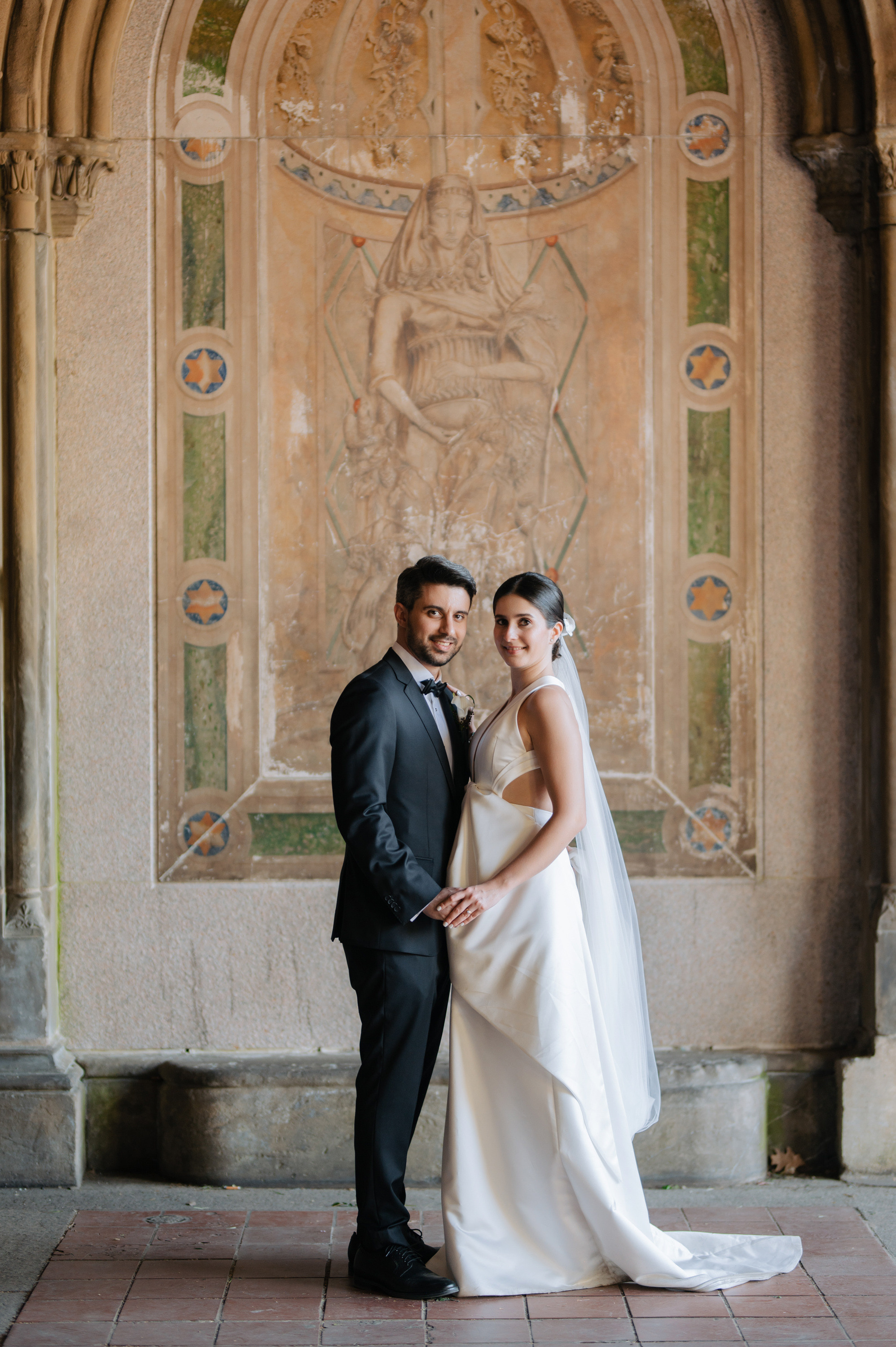 a bride and groom pose for a photo in front of a wall
