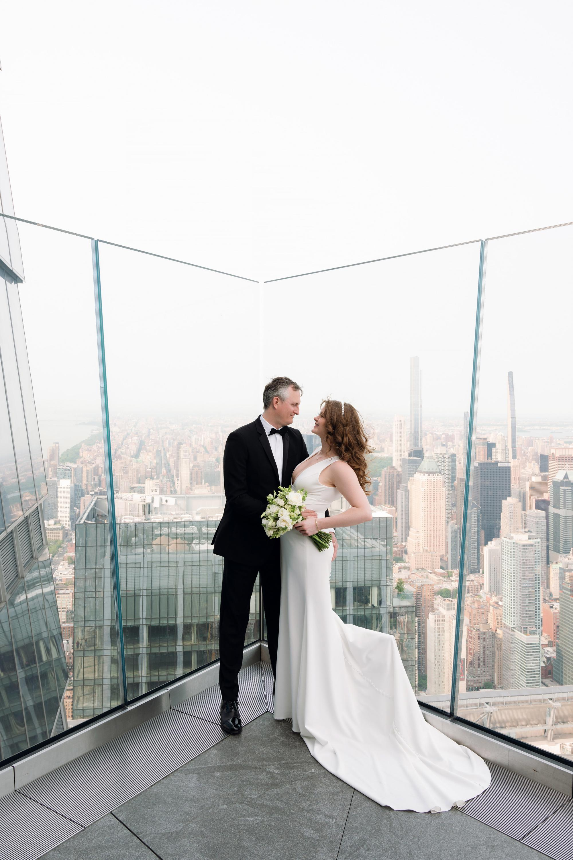a bride and groom standing on a rooftop overlooking of a city