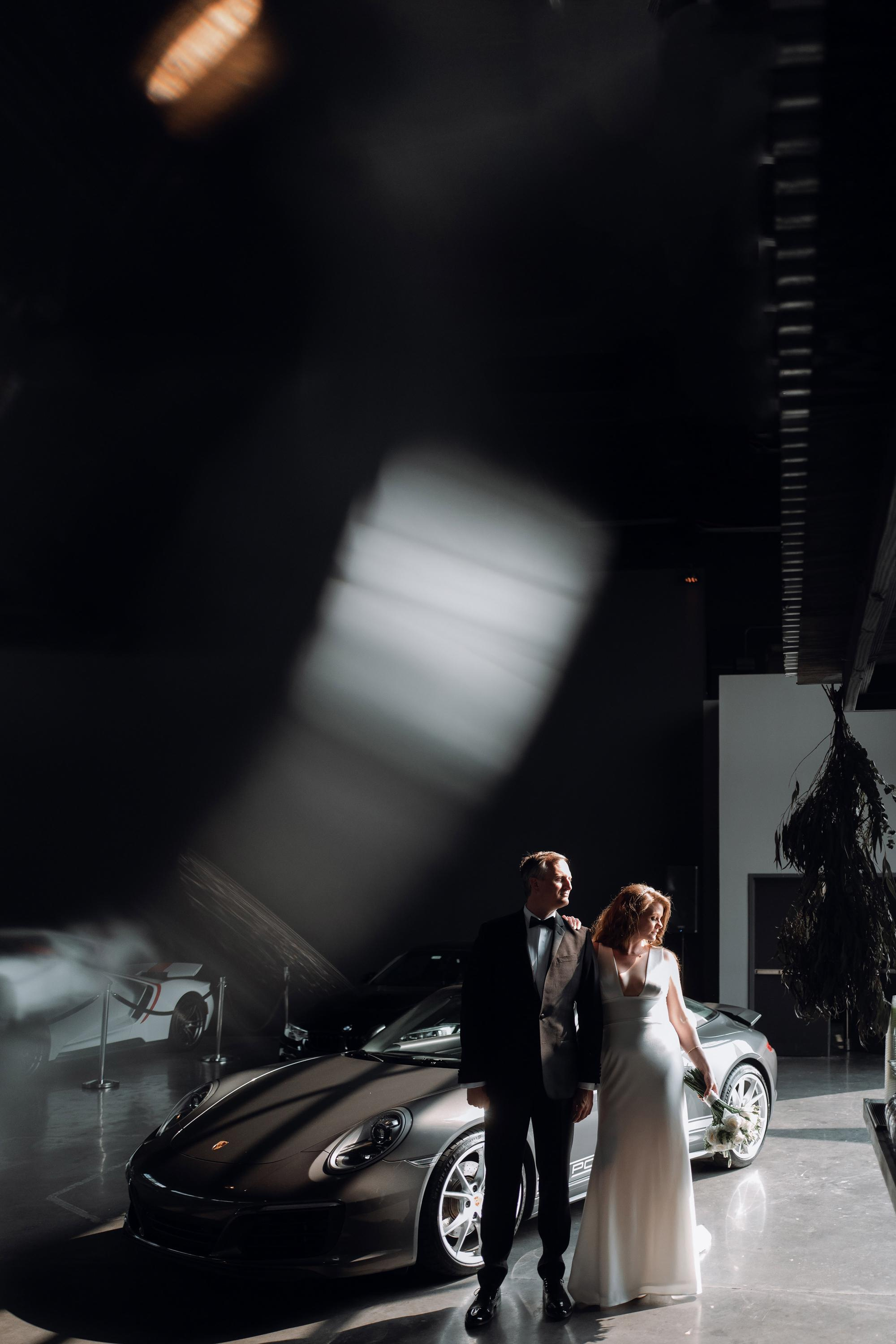 a bride and groom pose in front of a car