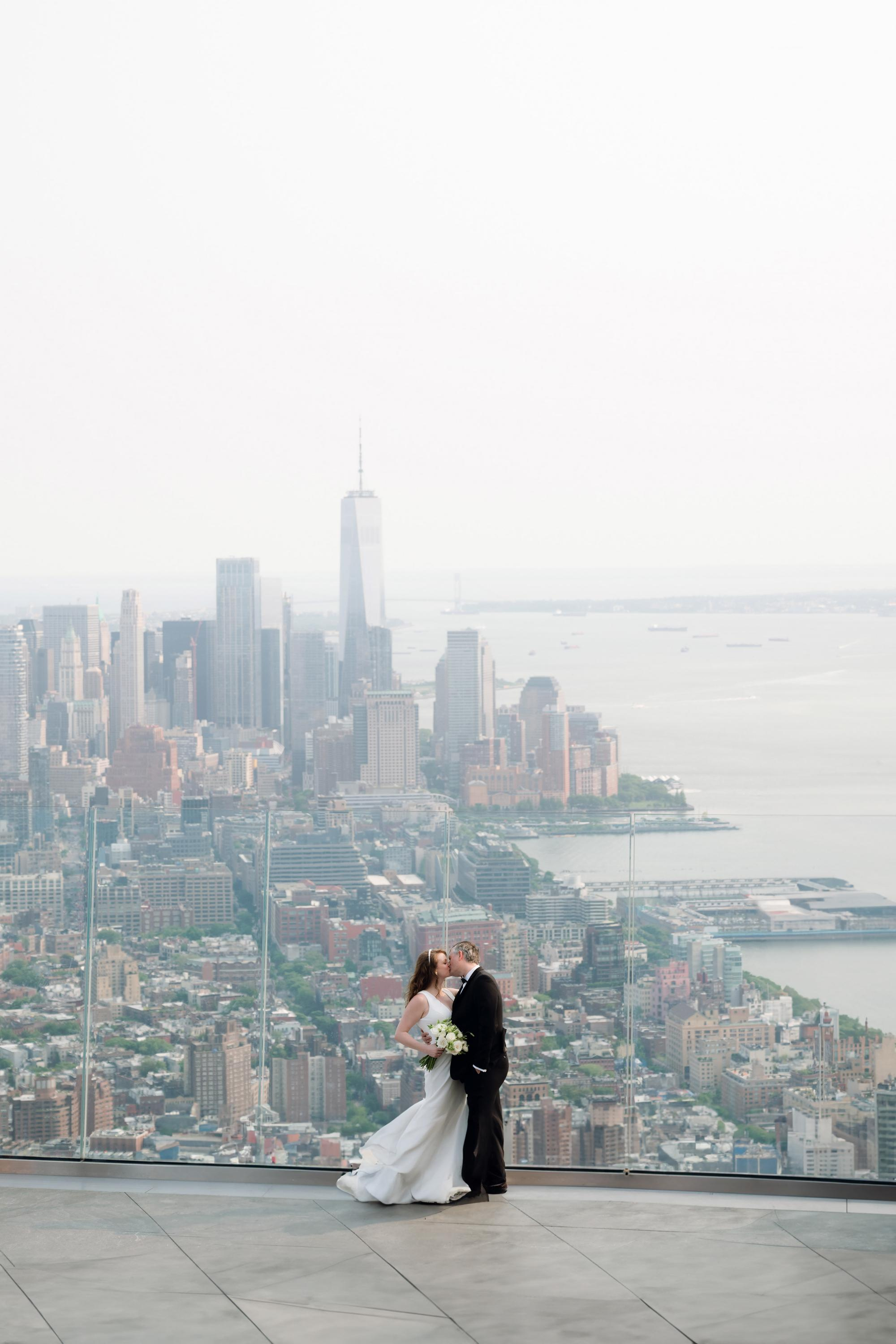 a bride and groom on the top of a building overlooking the city