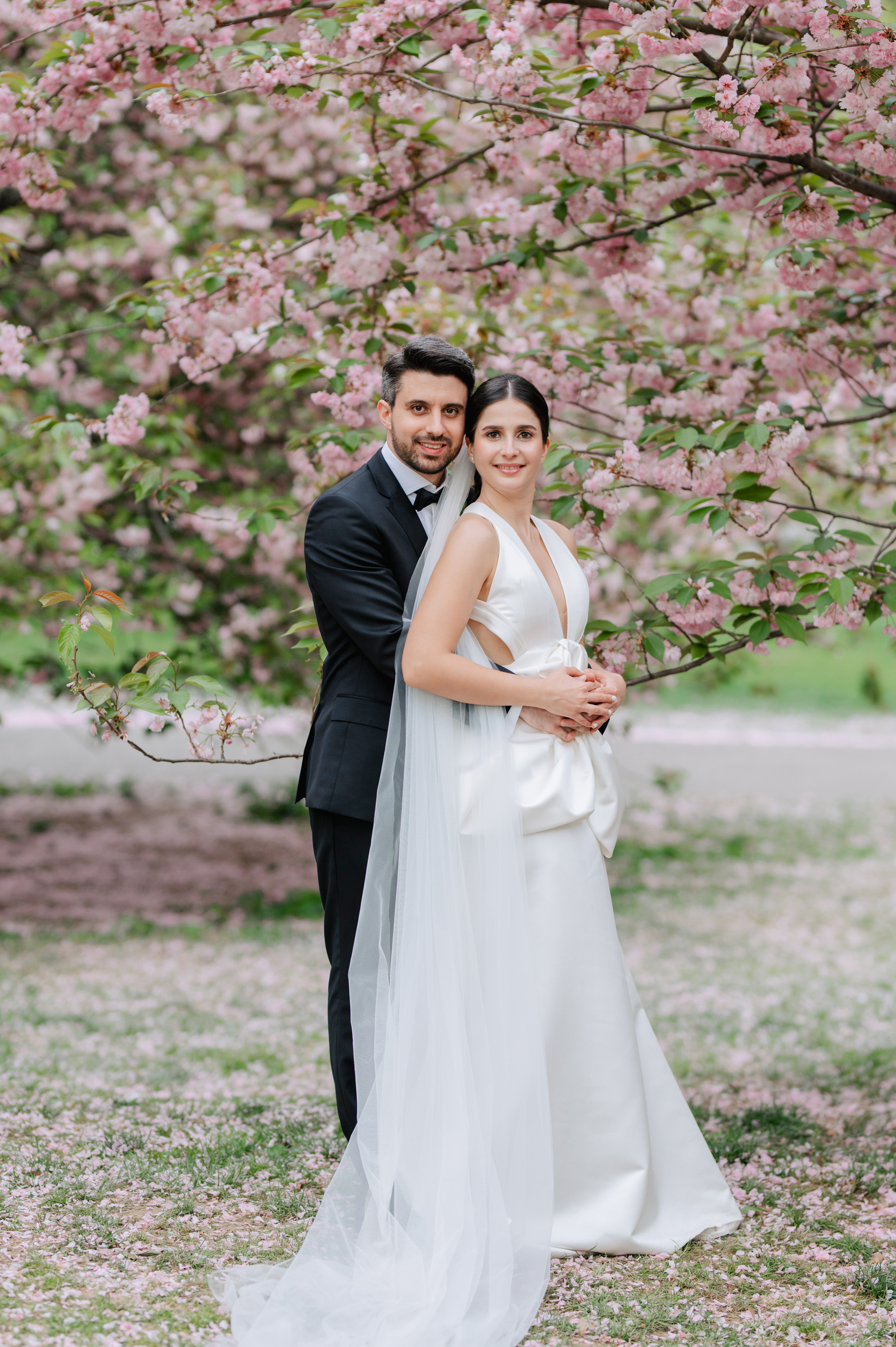 a bride and groom pose for a photo in front of a flowering tree
