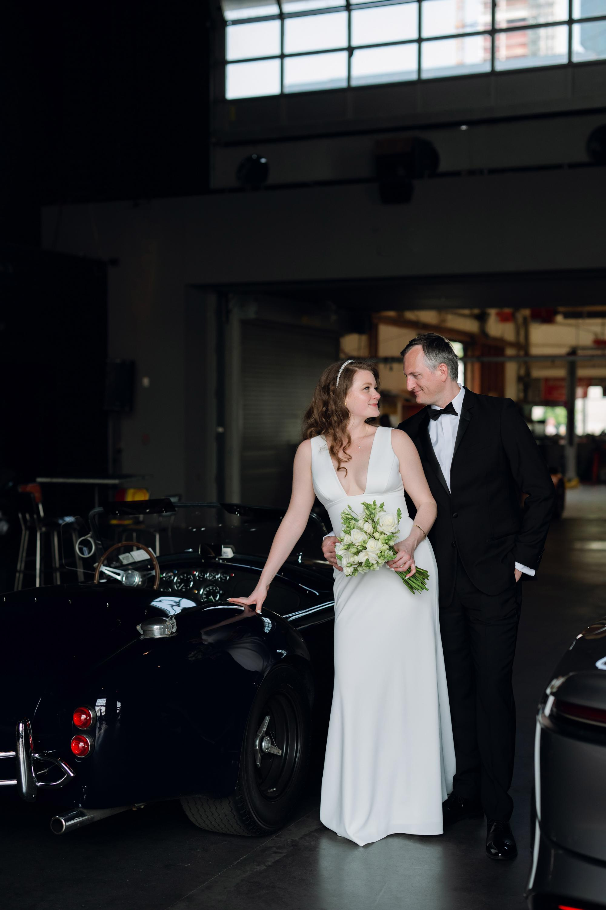 a bride and groom standing next to a black car