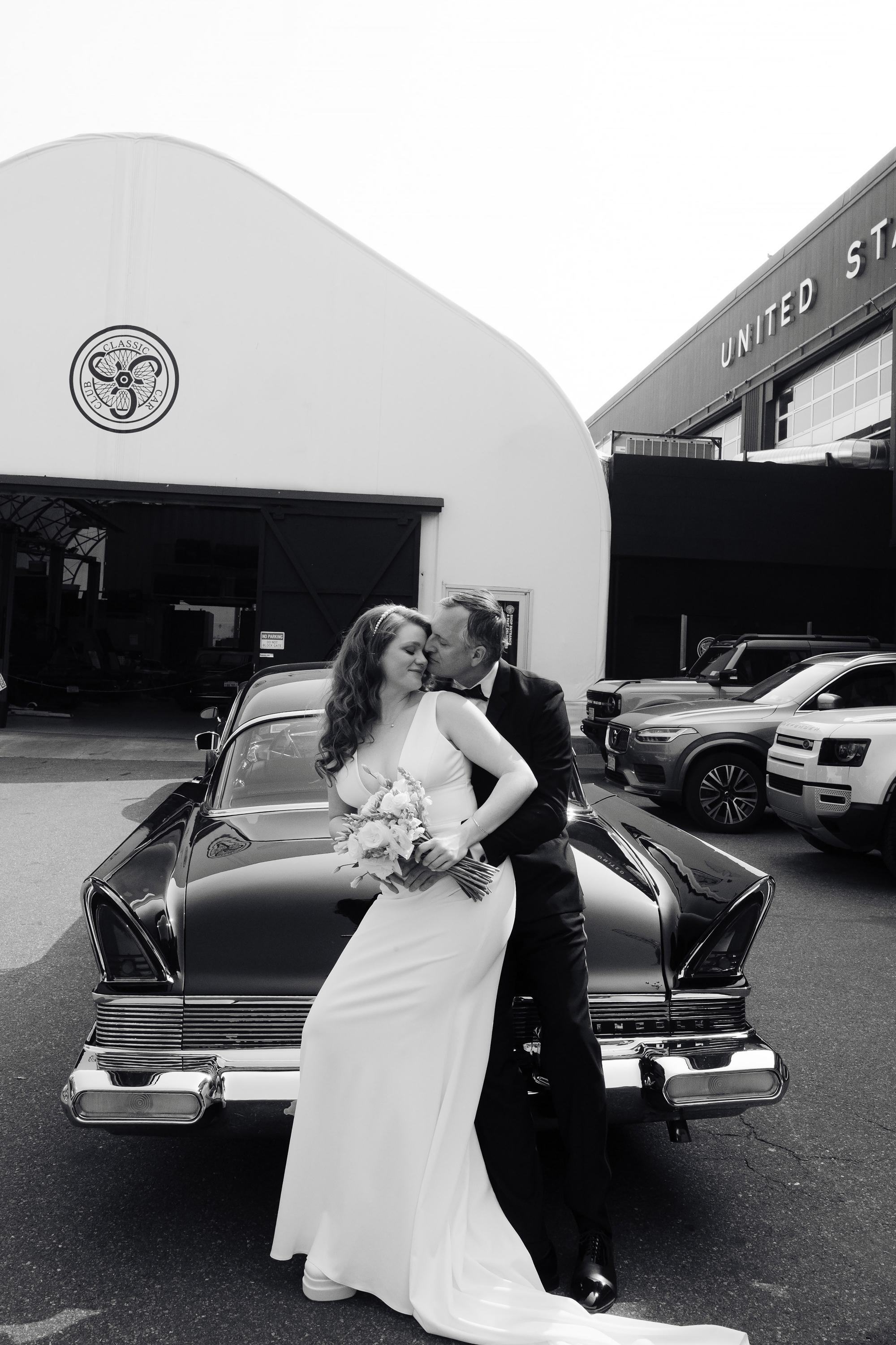 a bride and groom kissing in front of a car