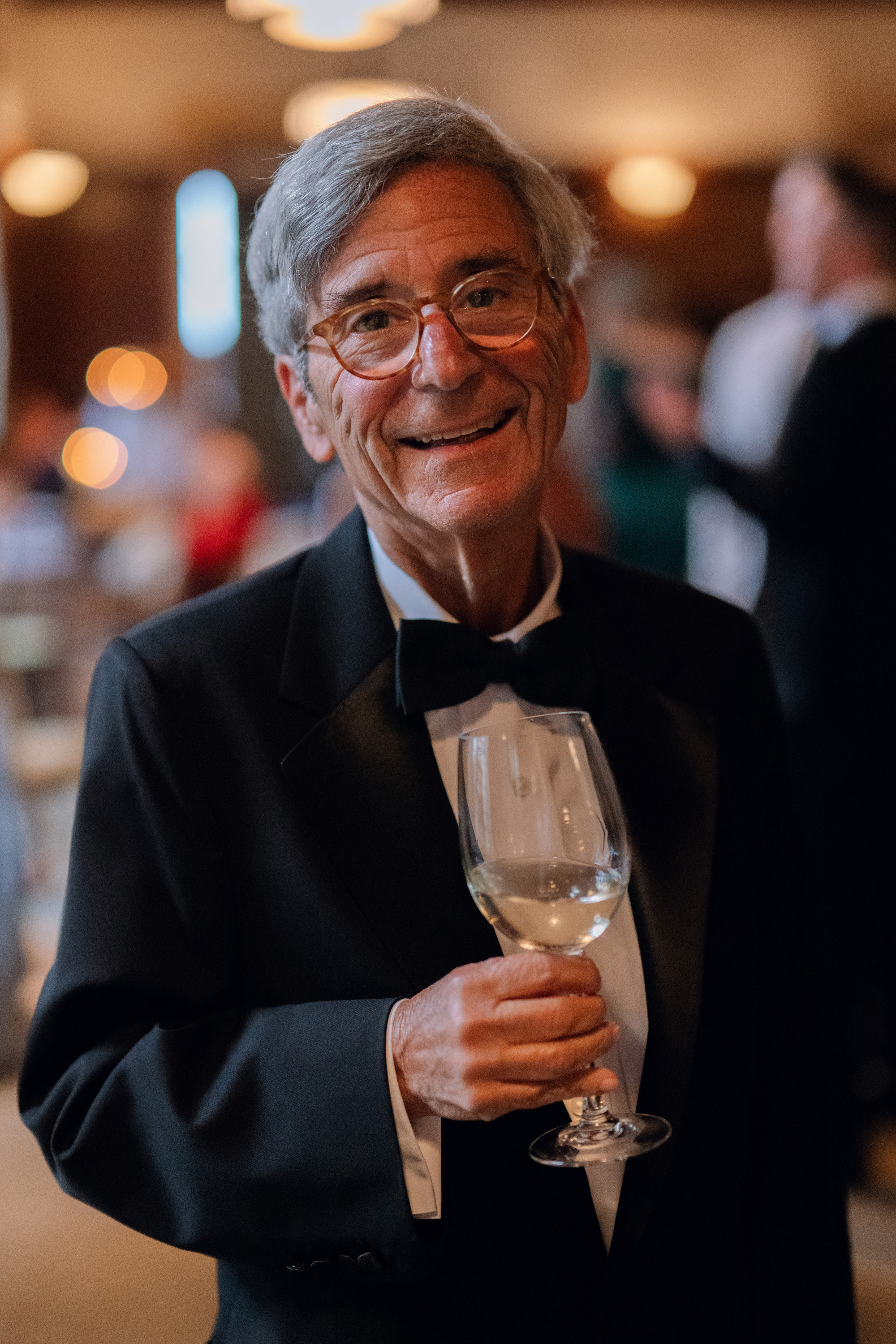 a man in a tuxed suit holding a glass of wine
