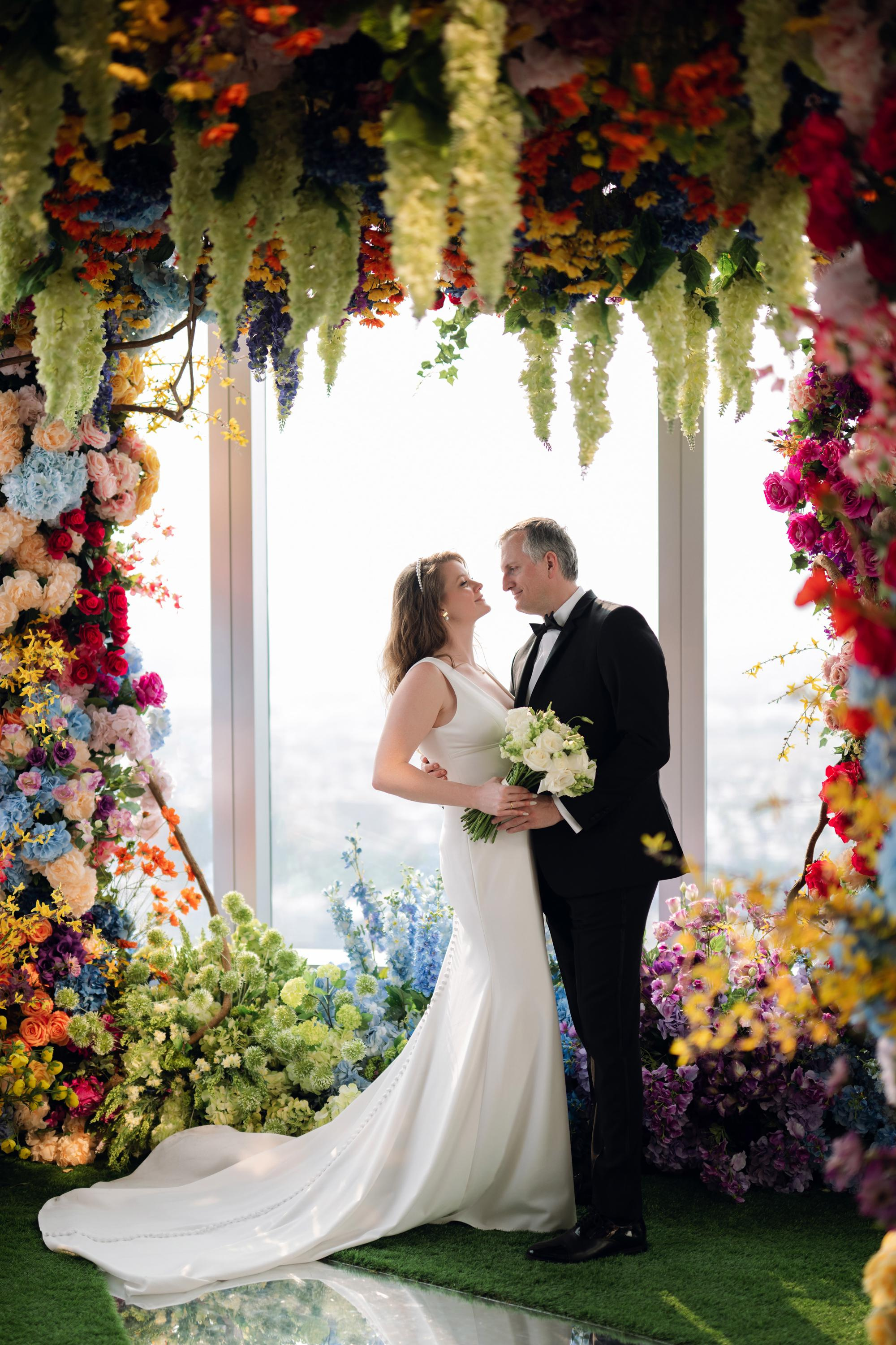 a bride and groom kissing in front of a colorful floral arch