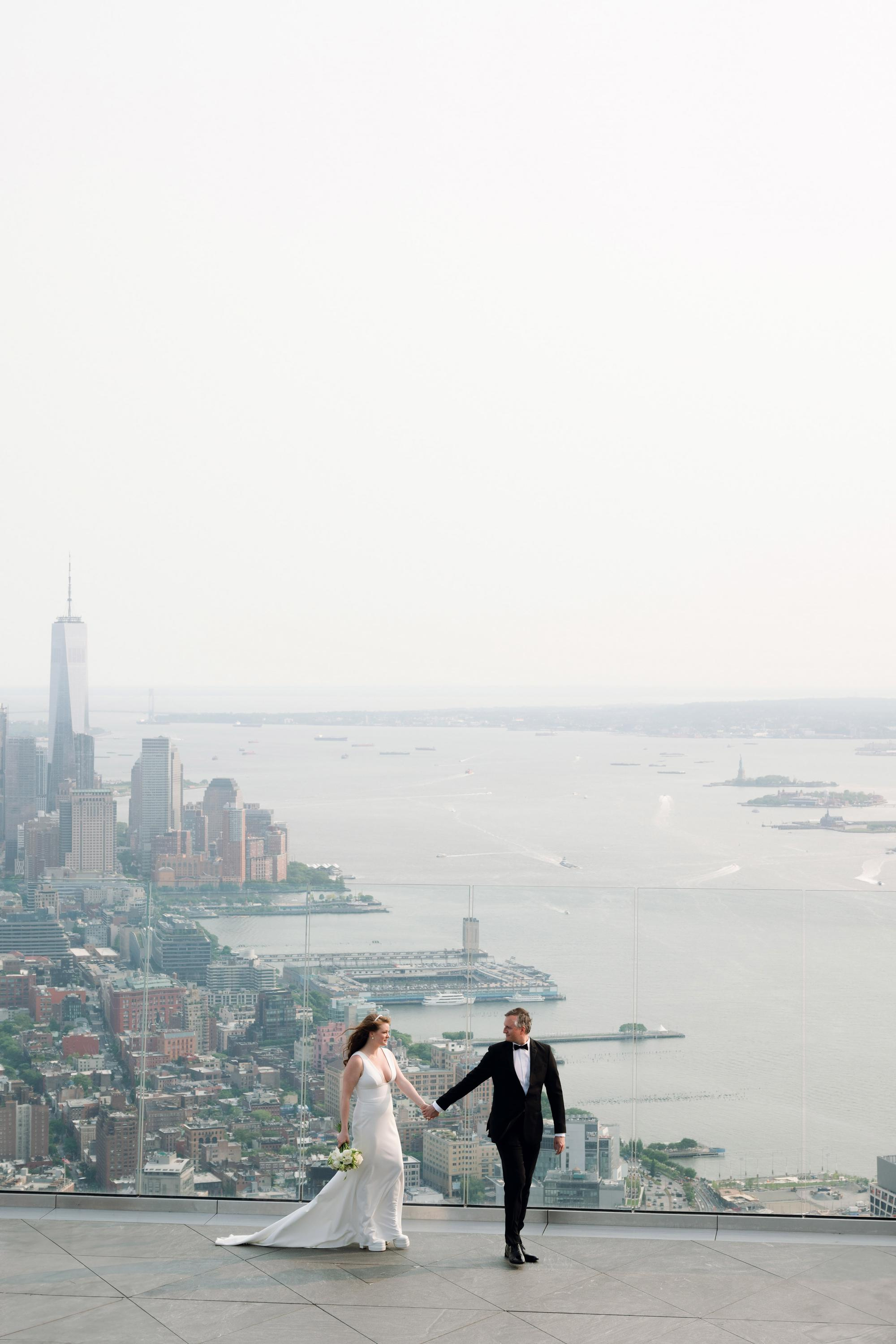 a bride and groom standing on a roof overlooking the city