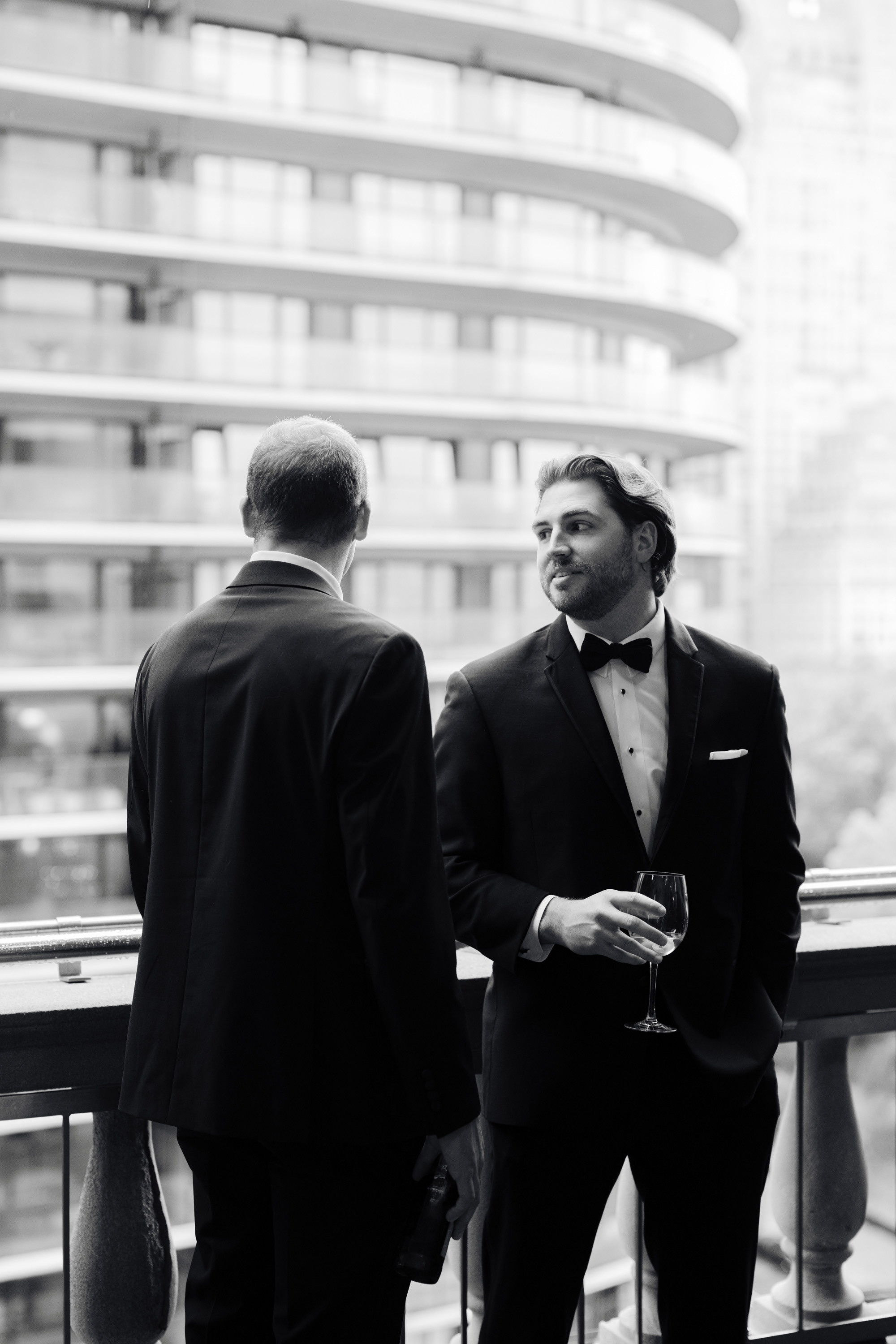 two men in suits are standing on a balcony
