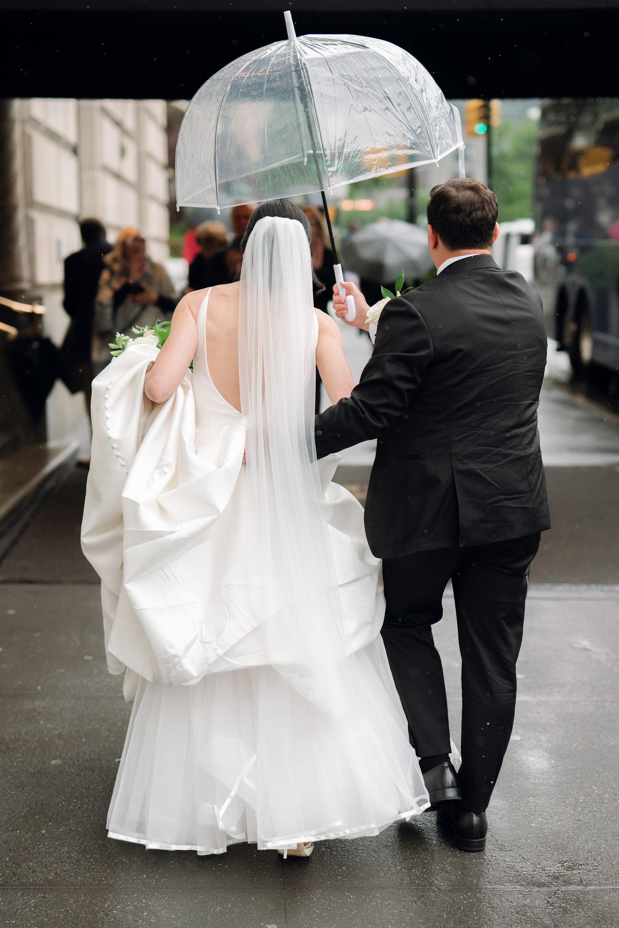 a bride and groom walking down the street holding umbrellas