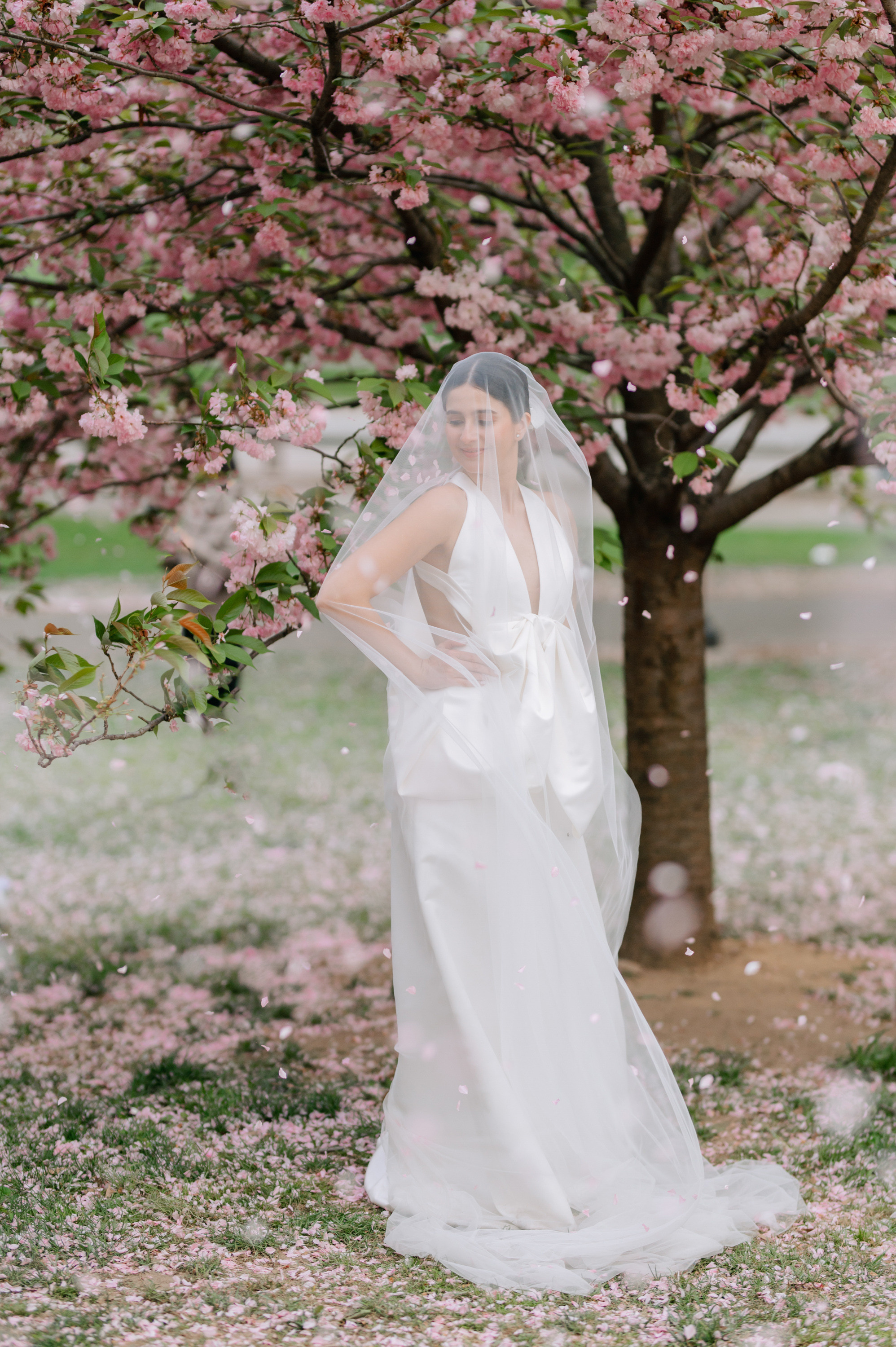 a bride in a white dress standing under a tree with pink flowers