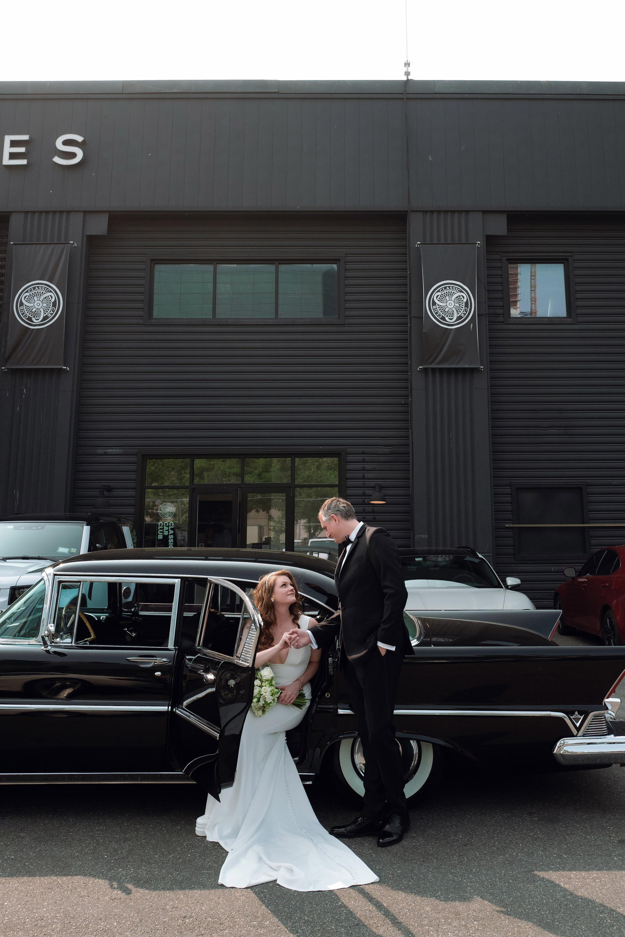 a bride and groom standing in front of a black car
