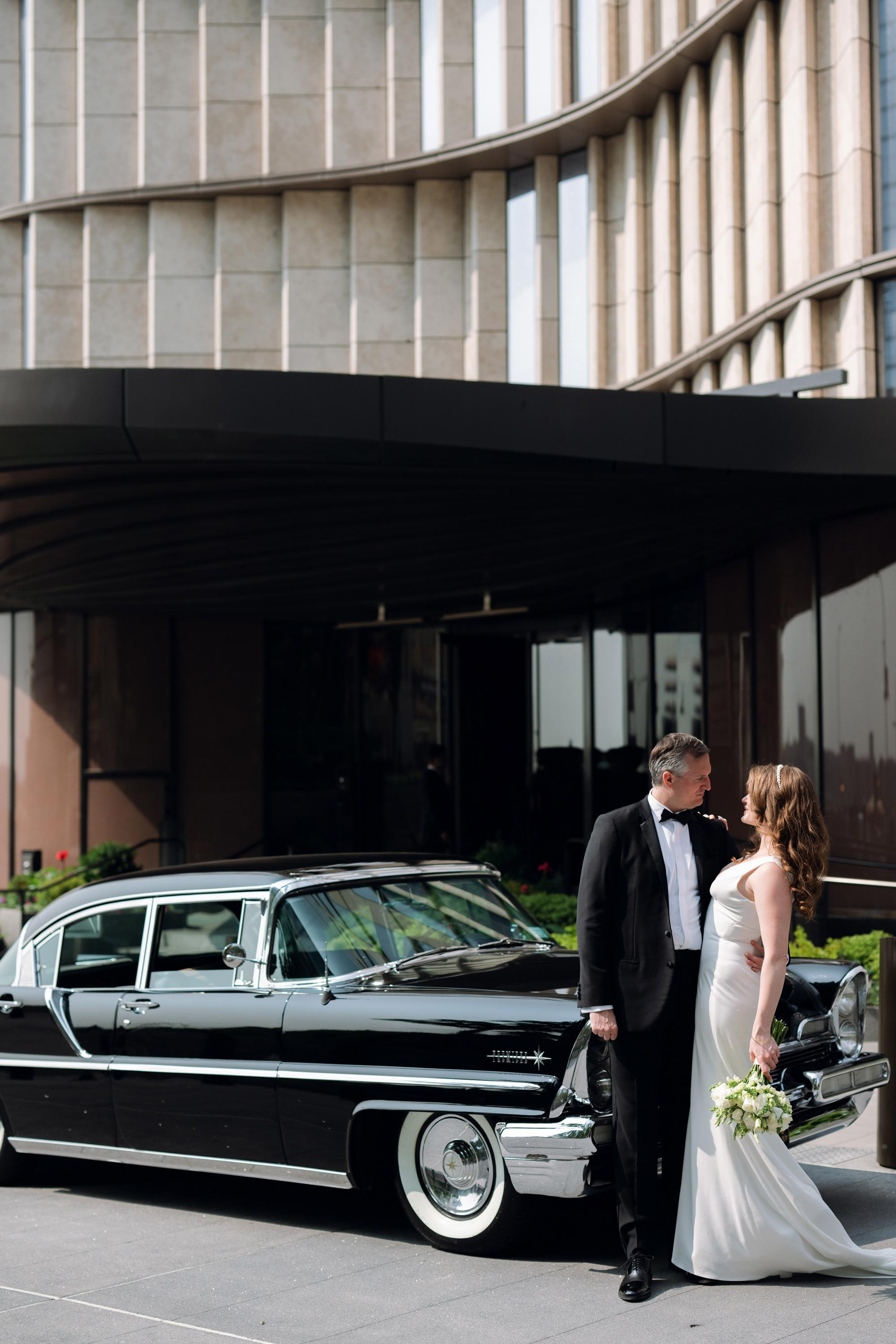 a bride and groom standing next to a black car