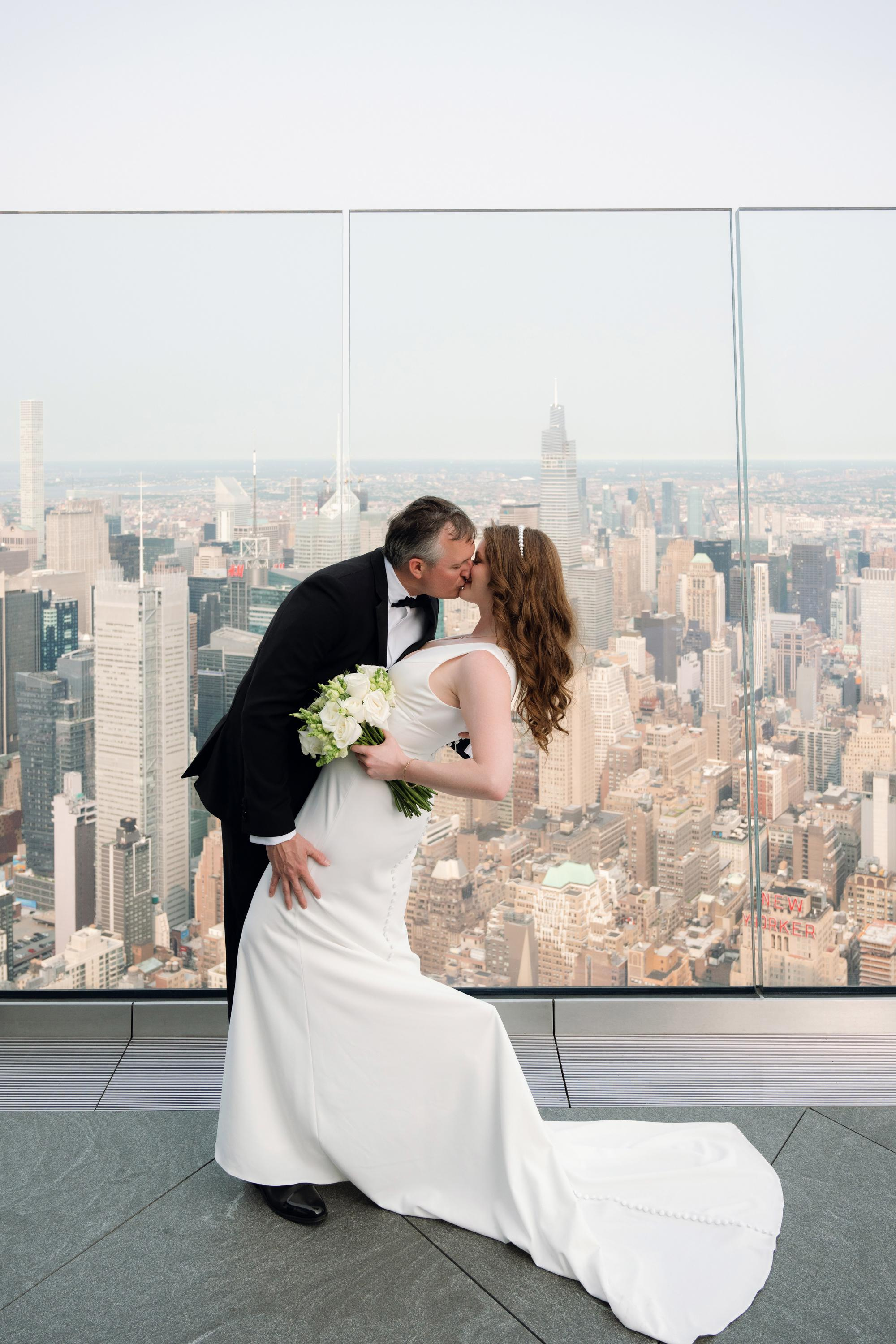 a bride and groom kissing in front of a cityscape
