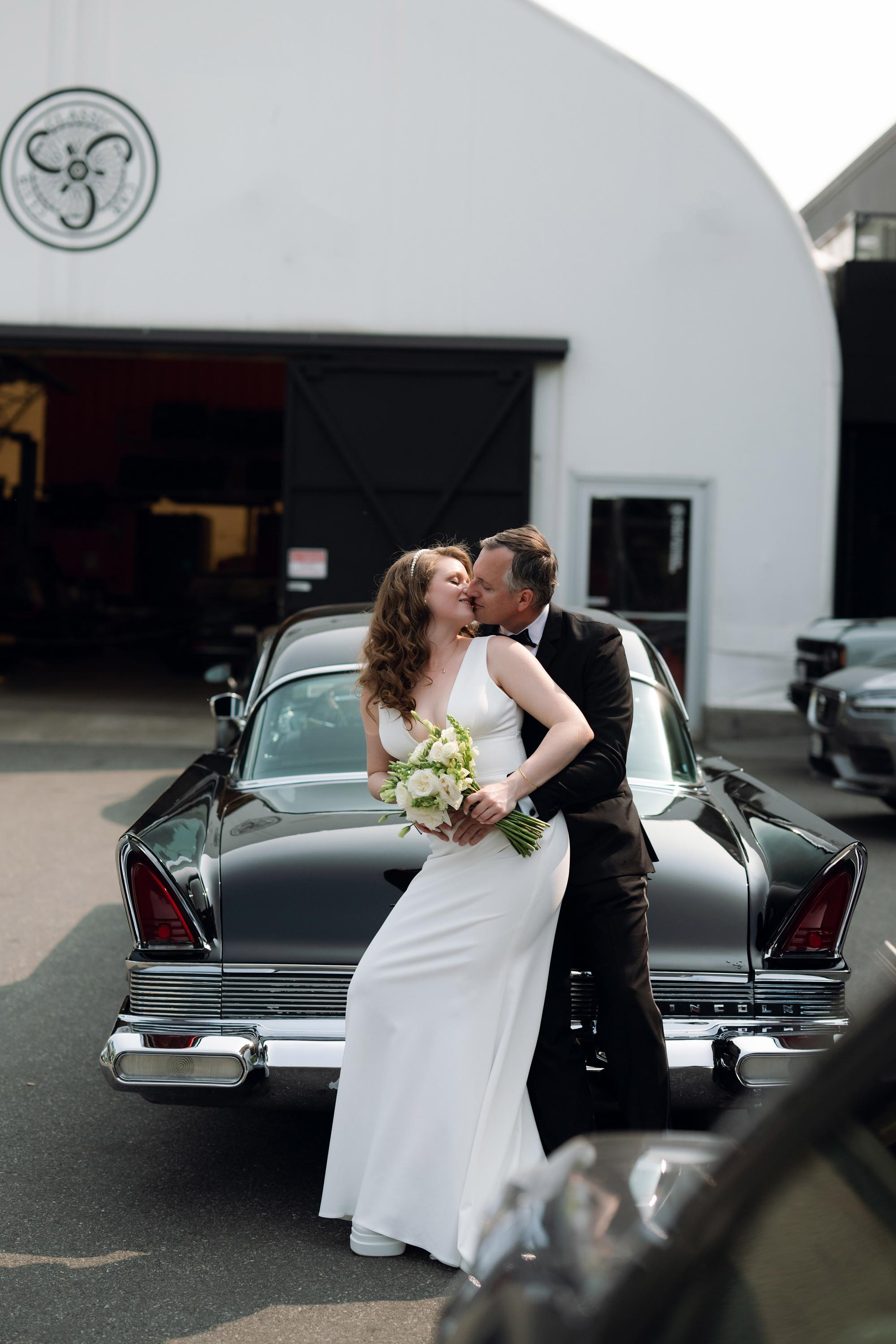 a bride and groom kissing in front of a black car