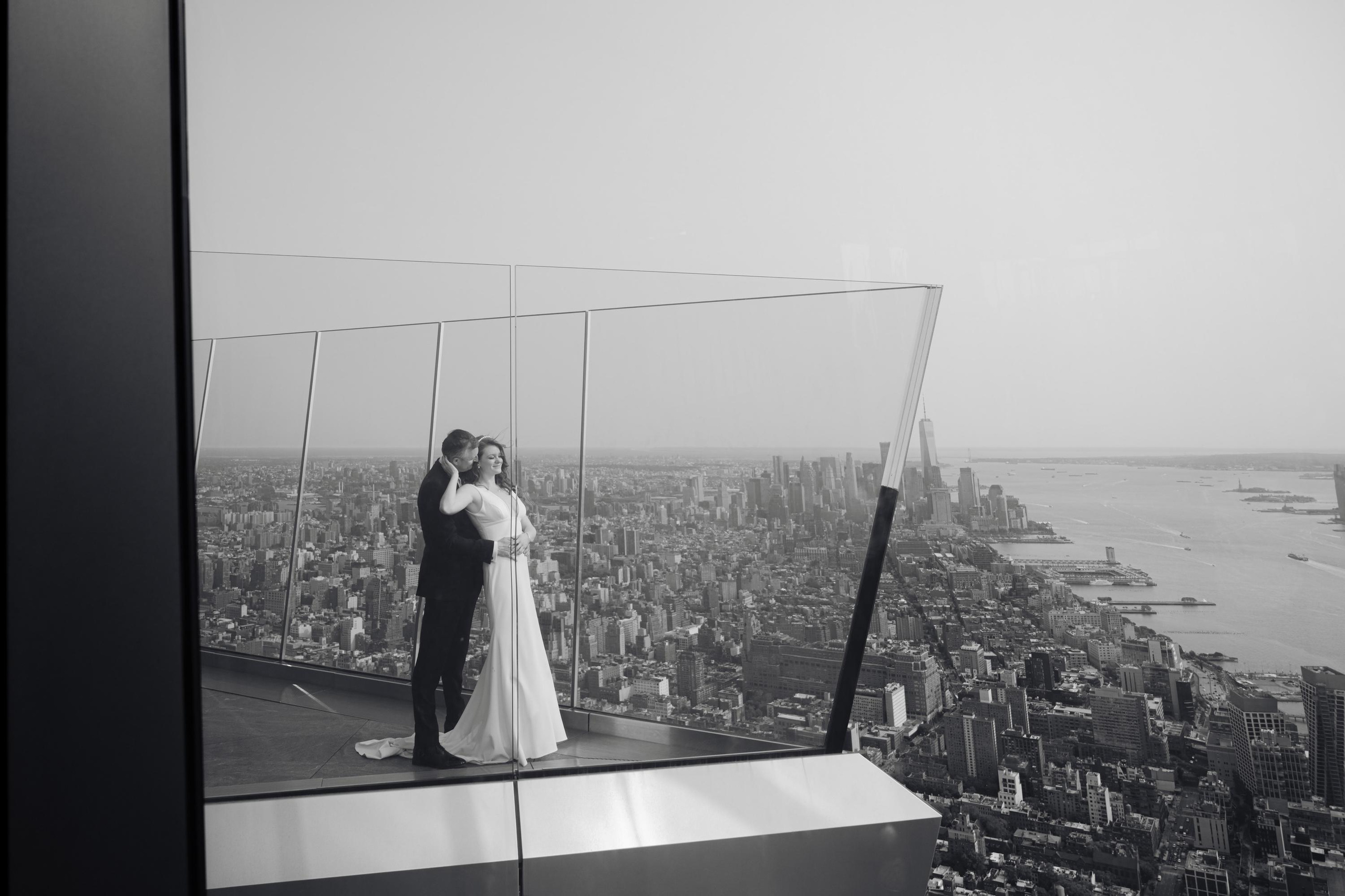 a bride and groom standing on the edge of a skyscraper