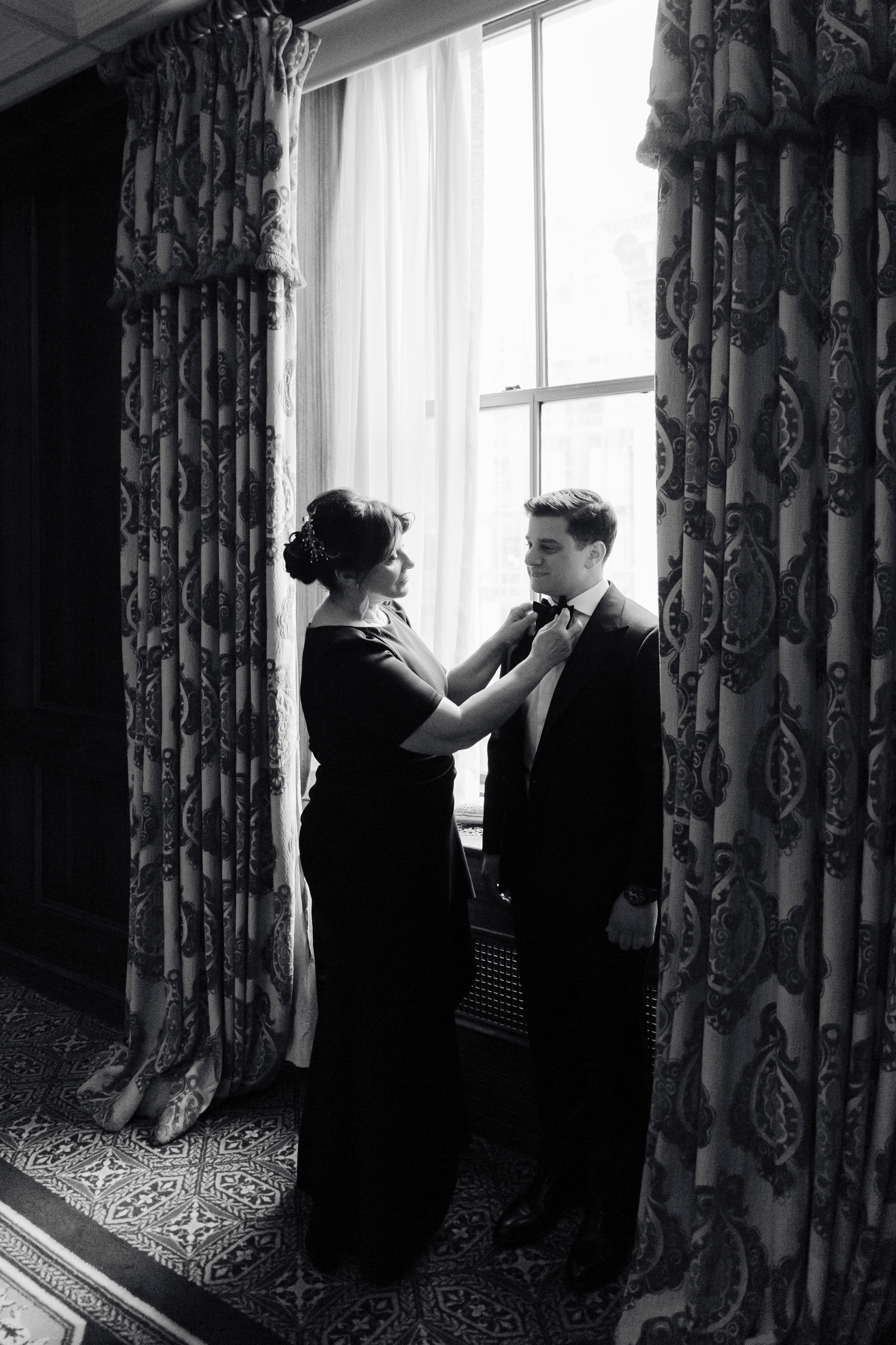 a man and woman in formal attire standing in front of a window