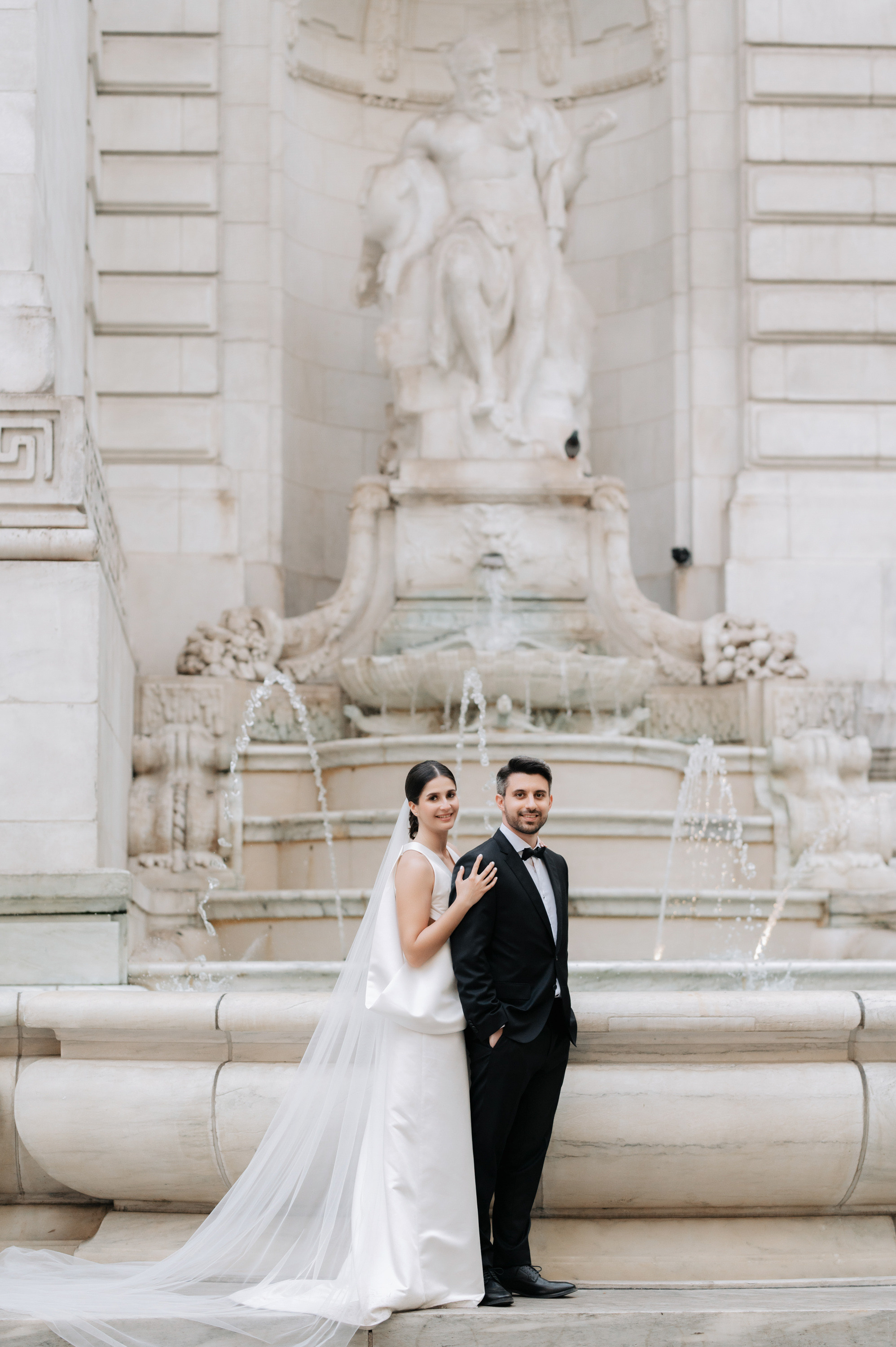 a bride and groom pose for a photo in front of the fountain