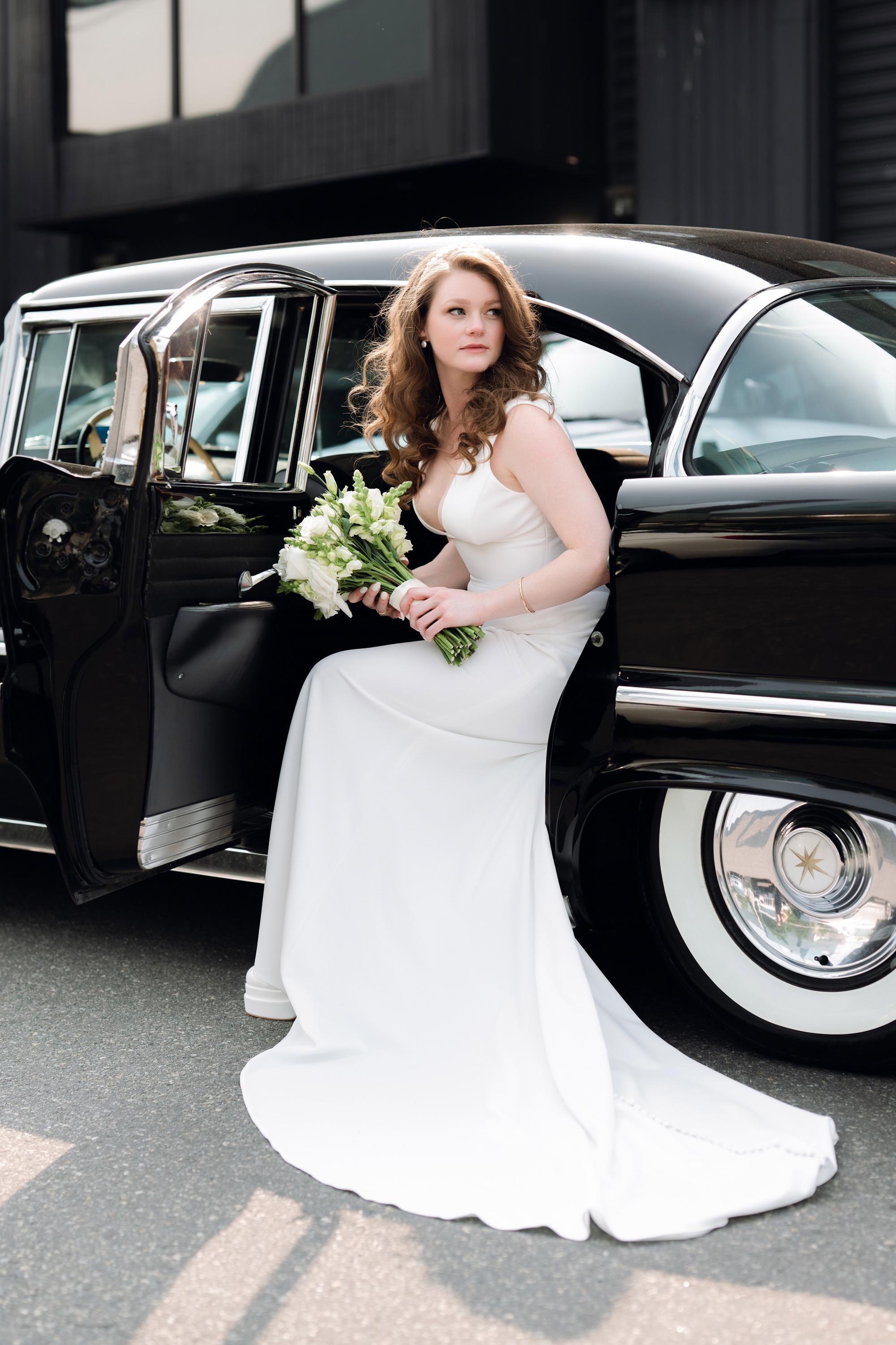 a bride in a white dress standing next to a black car