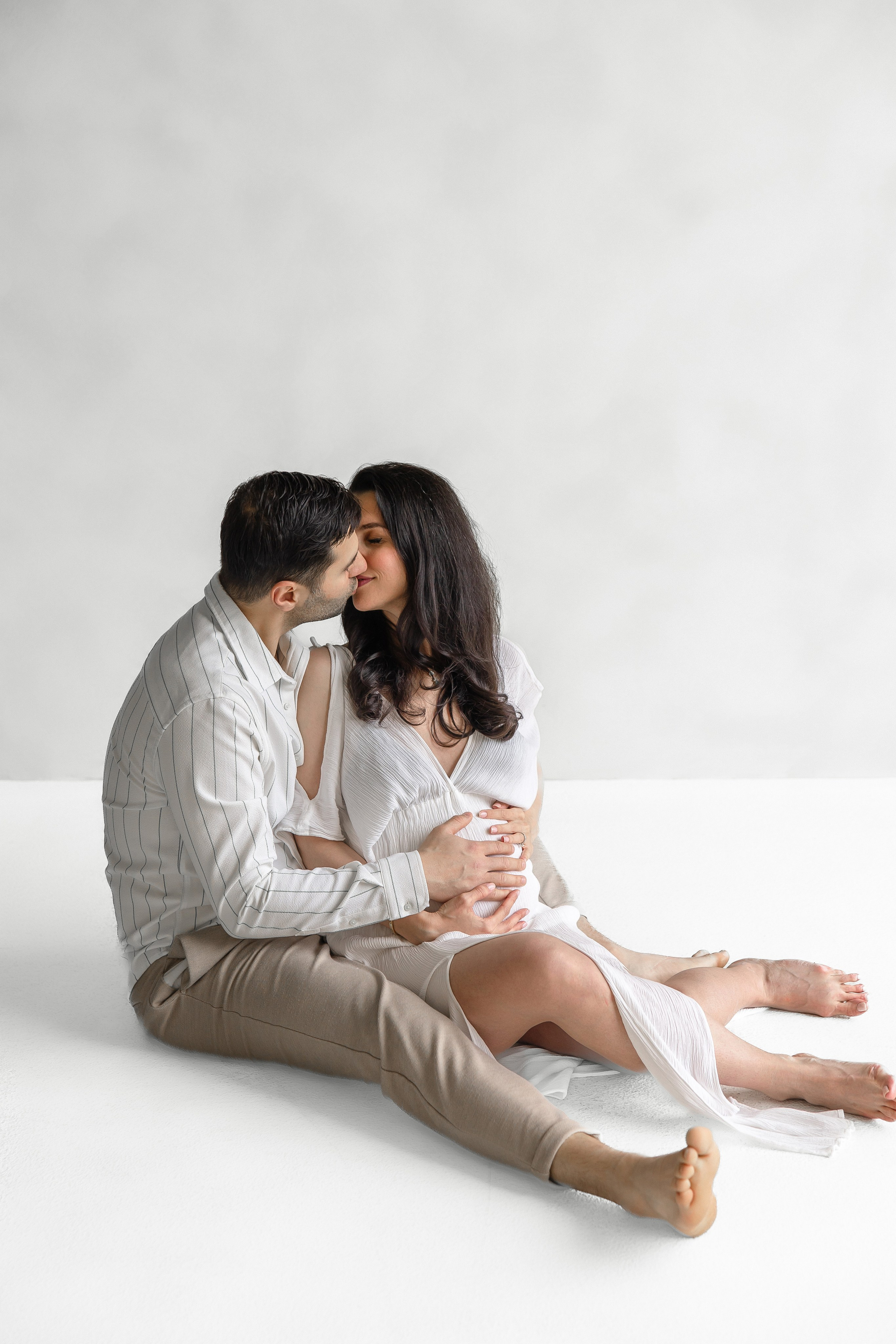 Pregnant couple kissing while sitting on the floor during a maternity photoshoot – romantic, modern pregnancy photography in Toronto by Iana Banana