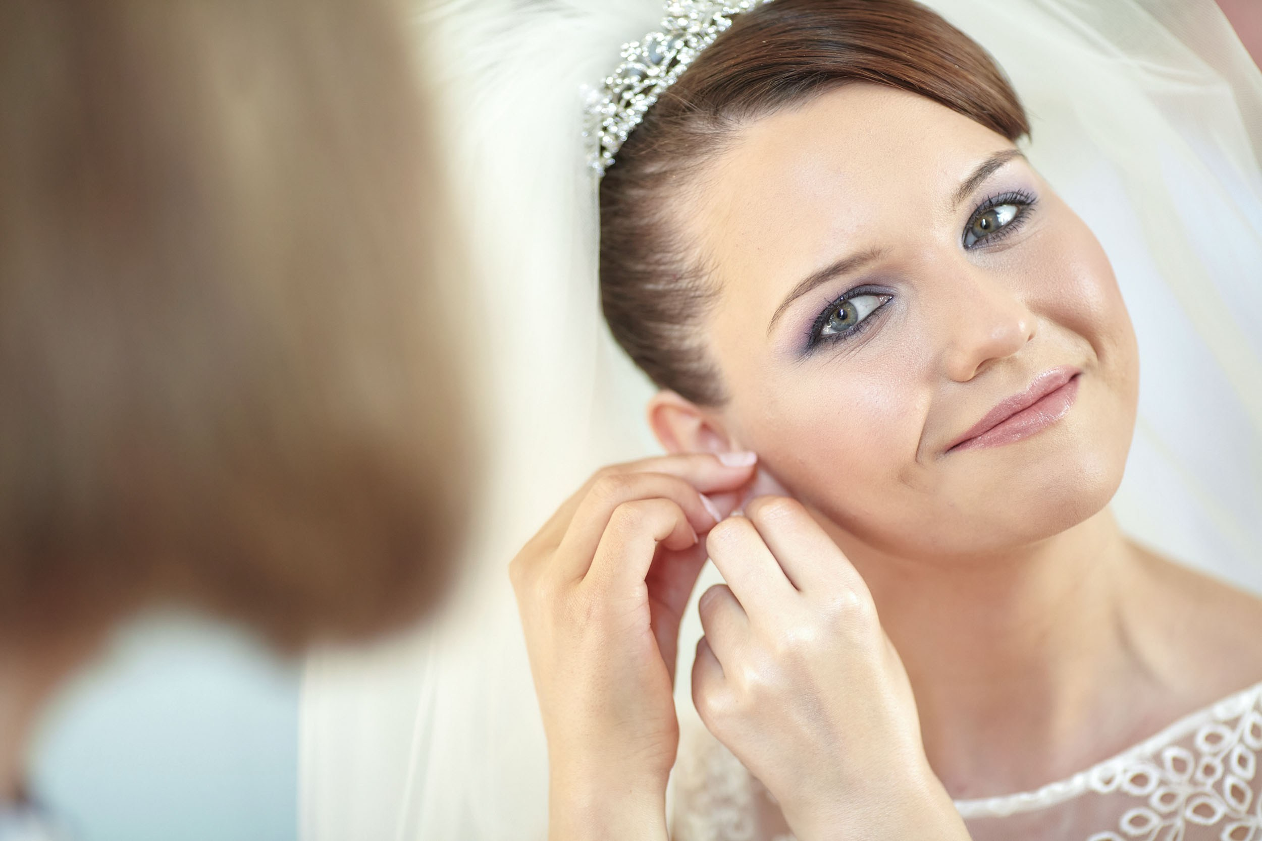 The young bride smiling at mirror while putting on earrings in Chateau Mcely bridal suite.