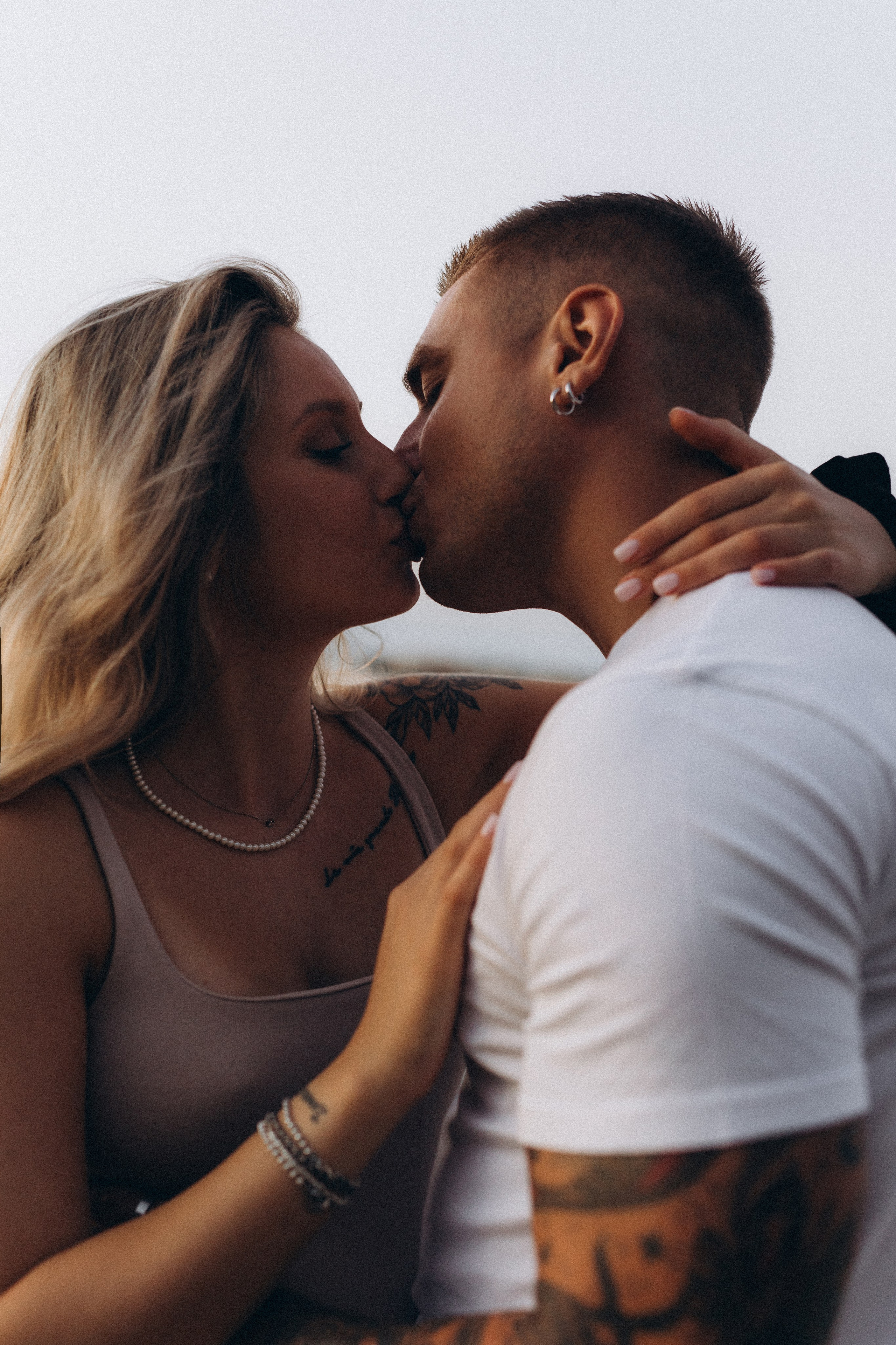 Coppia in attesa che si bacia teneramente durante un servizio fotografico maternity al mare al tramonto.