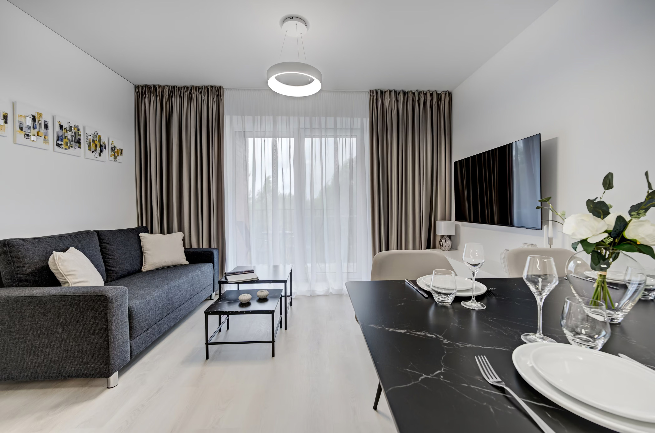 Svetainės interjeras: patogi sofa, juodi kavos staliukai ir stilinga valgomojo erdvė su serviruotu stalu.