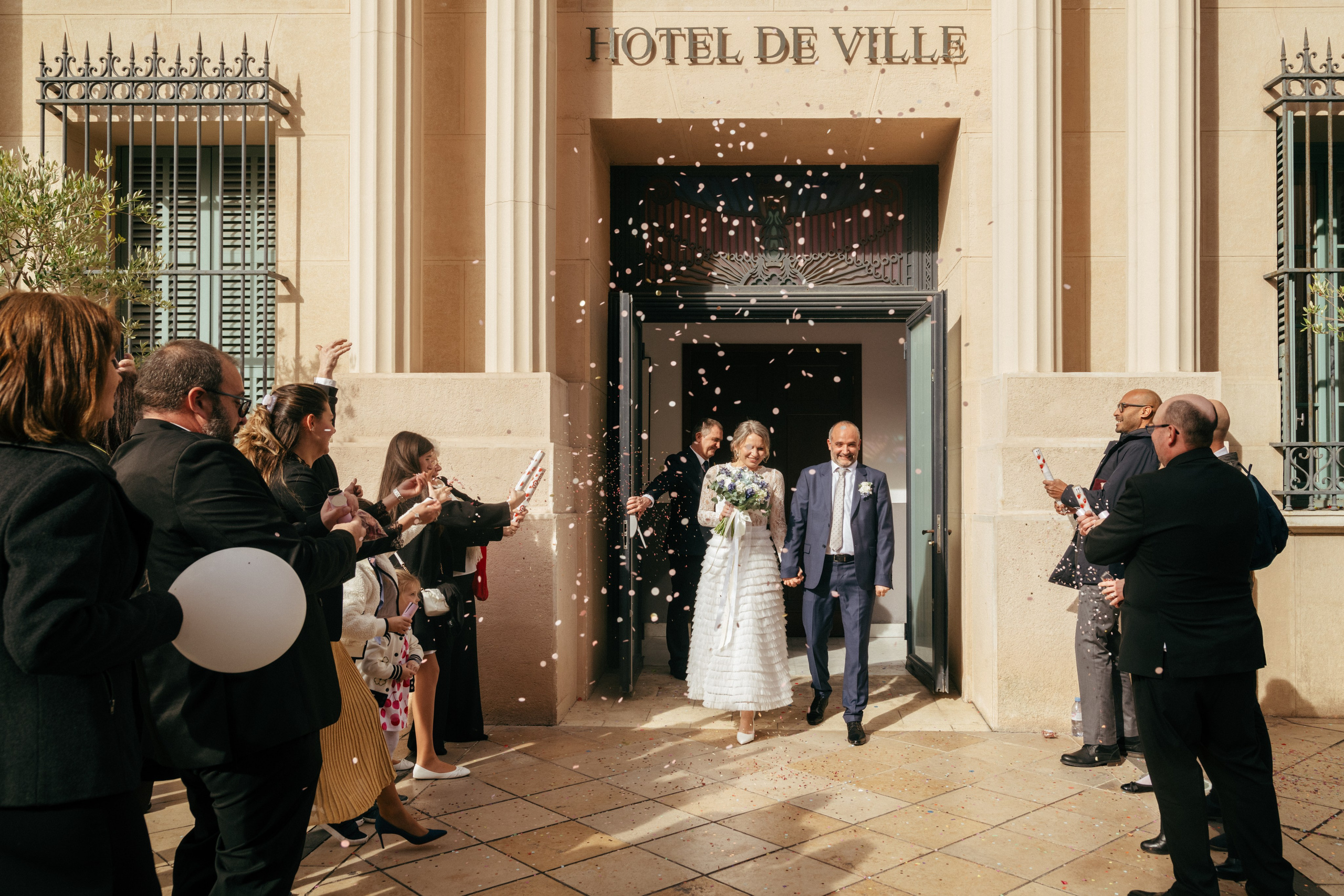 Les mariés sortent de la mairie pendant que les invités jettent des confettis.