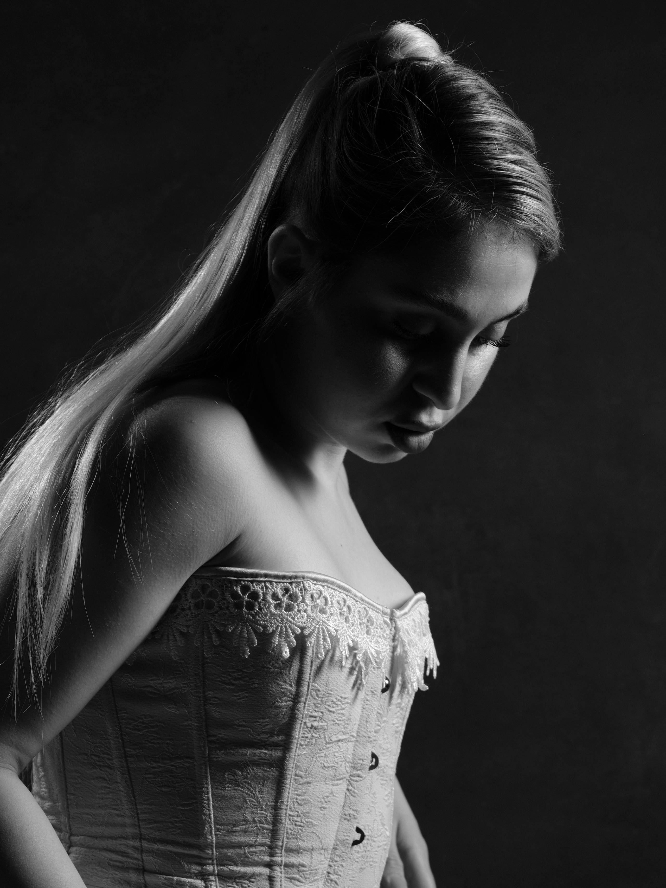 Minimalist studio portrait of a woman in a corset, black and white fashion photography with dramatic light and shadow.