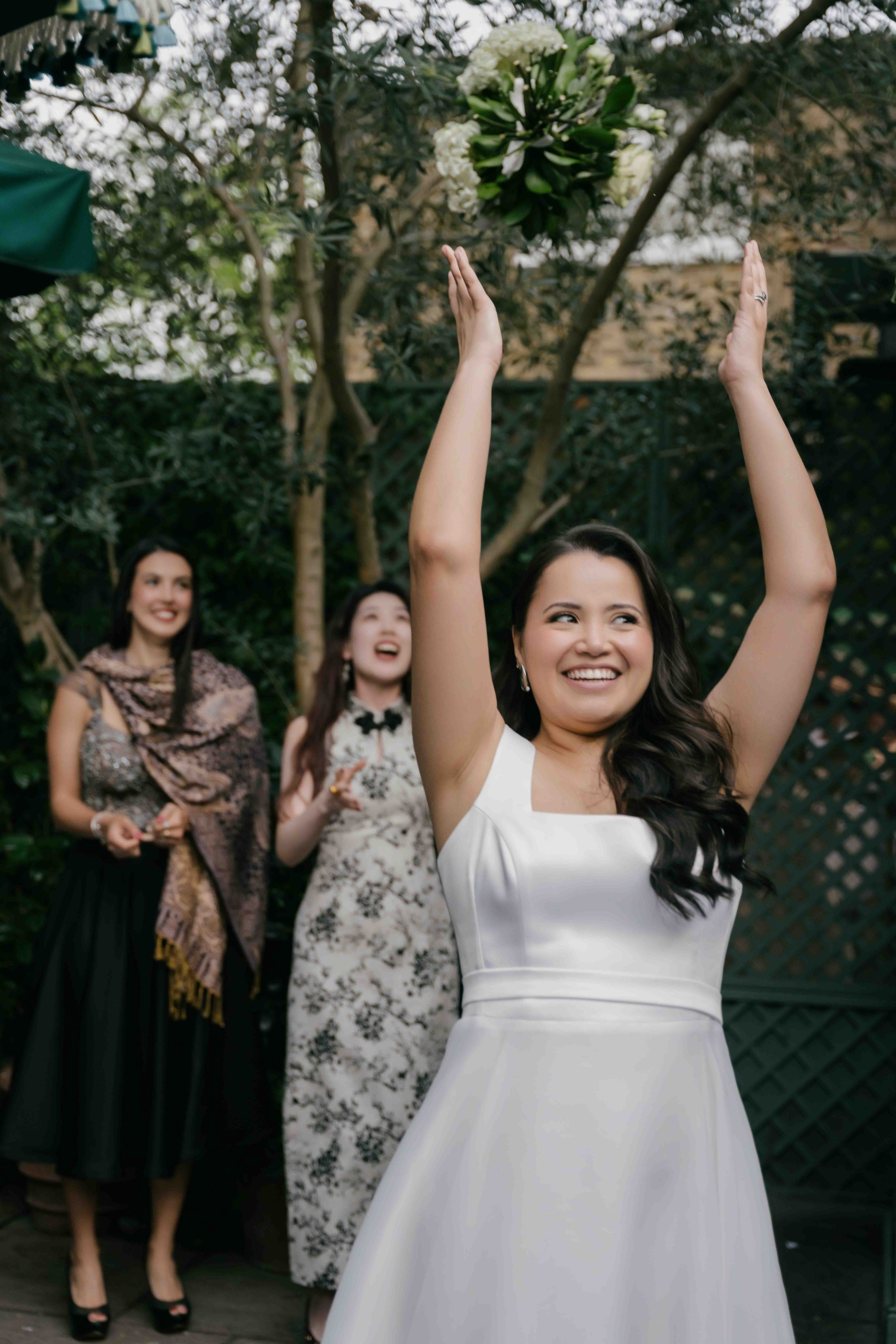 Bride throwing bouquet at wedding reception in London, joyful moment with guests, elegant and natural wedding photography