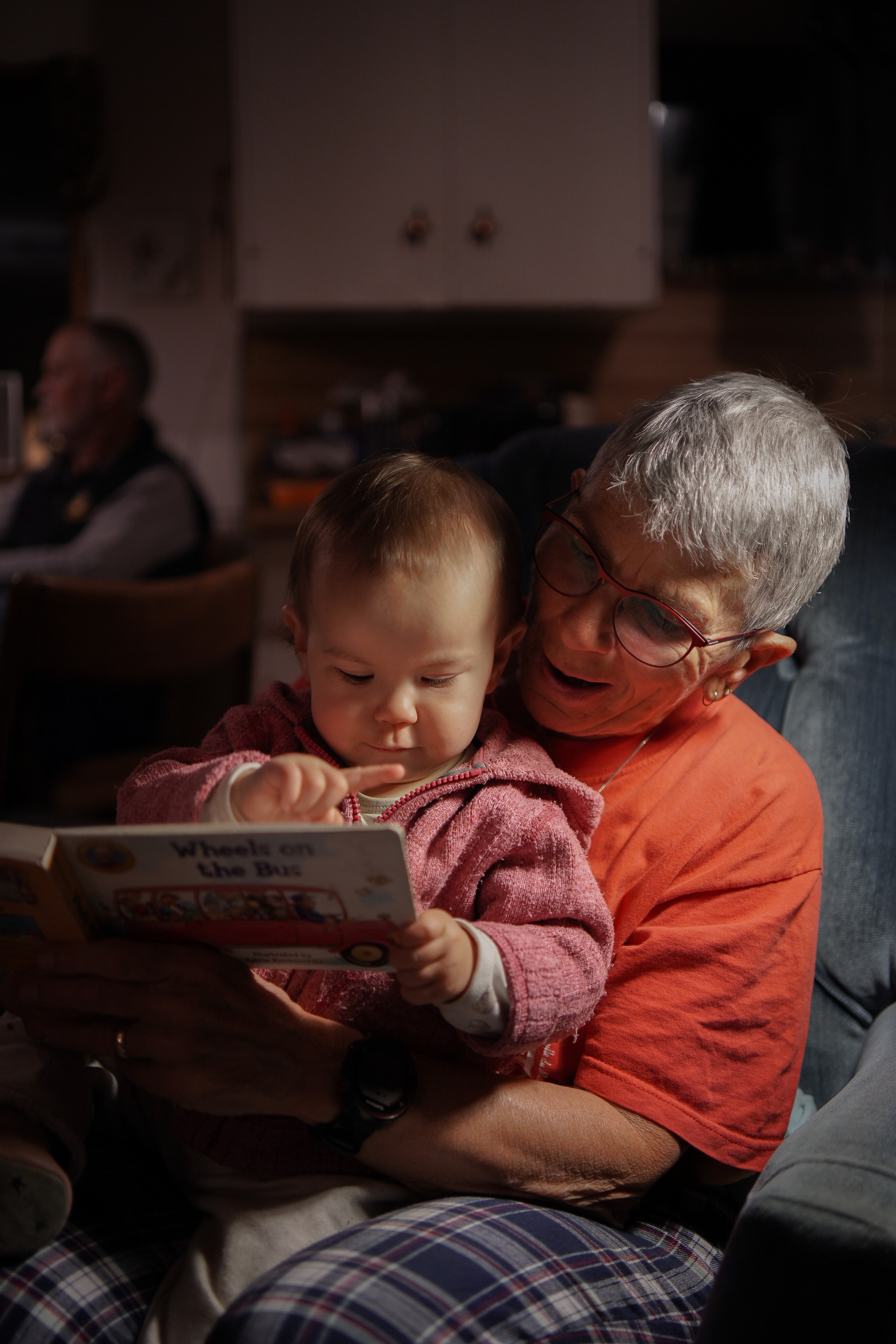 Grandmother holding her granddaughter on her lap, while reading her a book