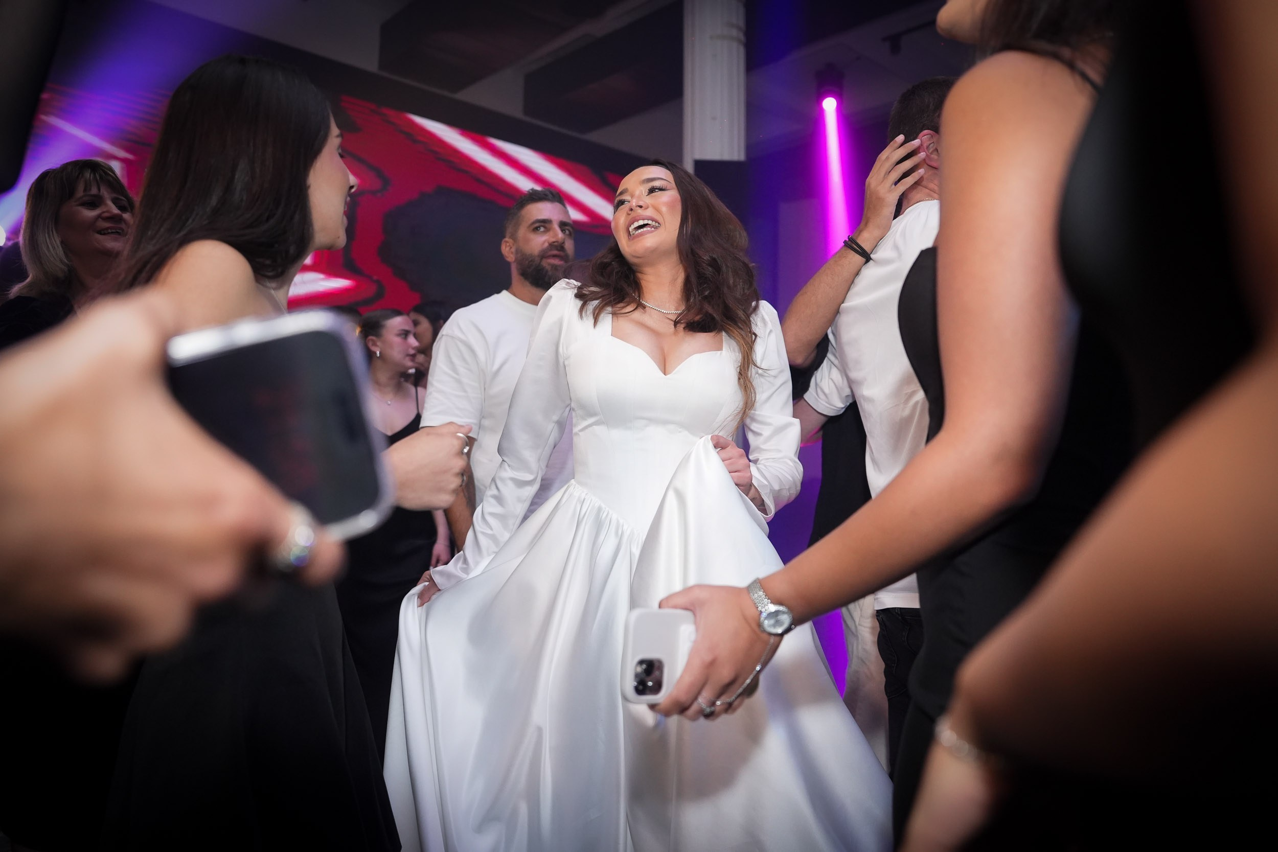 A bride laughs and dances surrounded by wedding guests