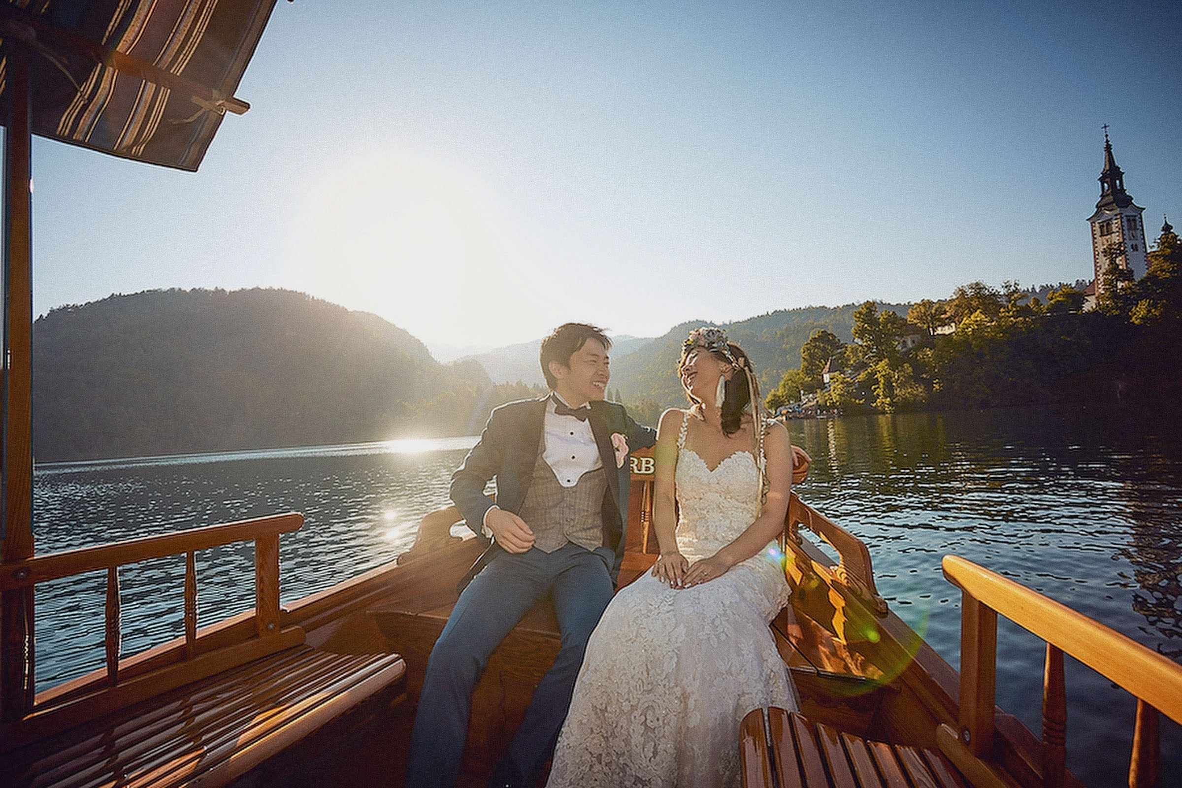 Romantic scene of a Japanese bride and groom as they enjoy a private boat ride as the sun is seen from behind them.