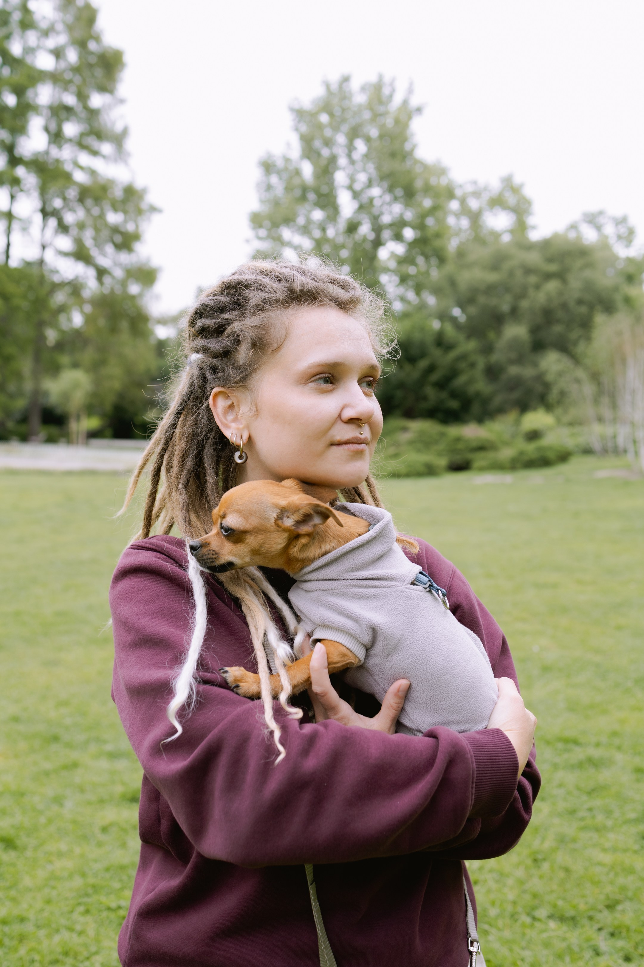 Юля с дредами задумчиво смотрит в сторону, зелёный фон парка.