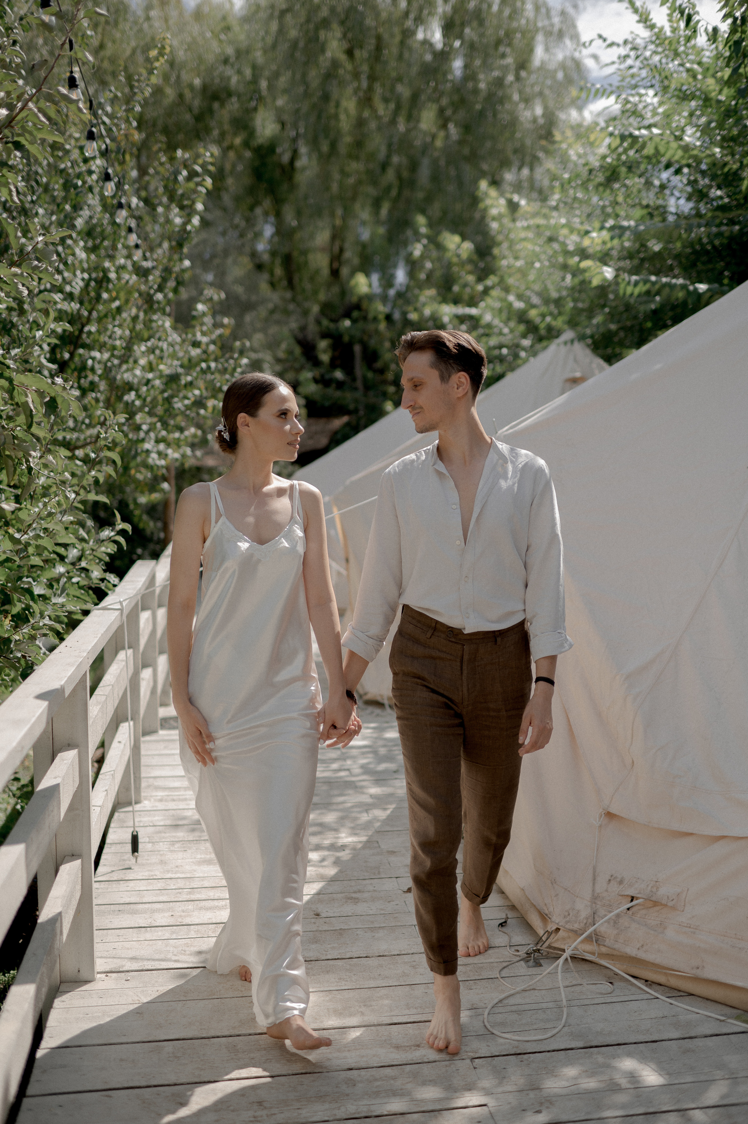 In a secluded garden retreat, the couple's wedding morning unfolds in the cozy embrace of glamping tents, creating an intimate atmosphere for their loving connections and tender exchanges.