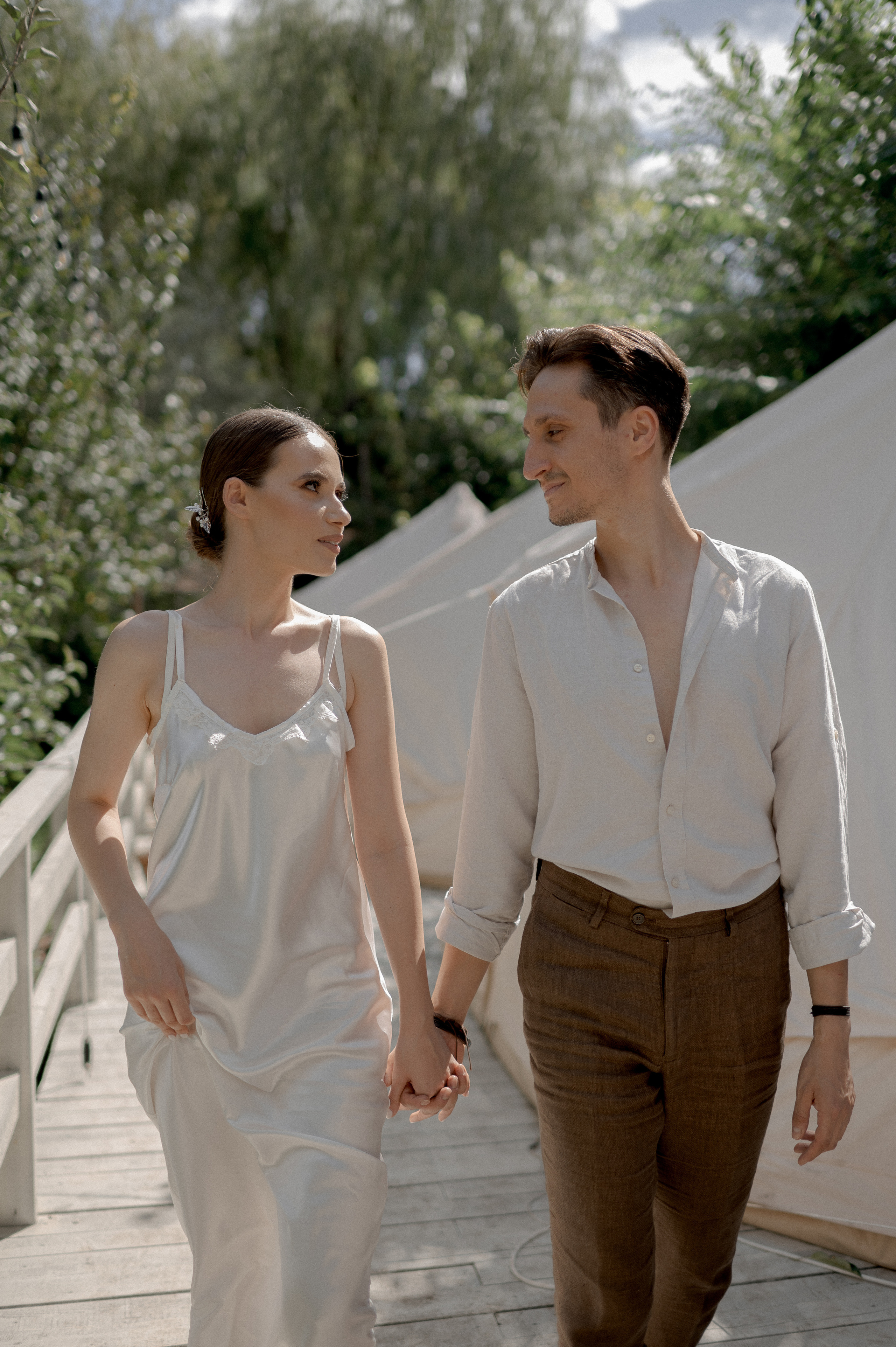 In a secluded garden retreat, the couple's wedding morning unfolds in the cozy embrace of glamping tents, creating an intimate atmosphere for their loving connections and tender exchanges.