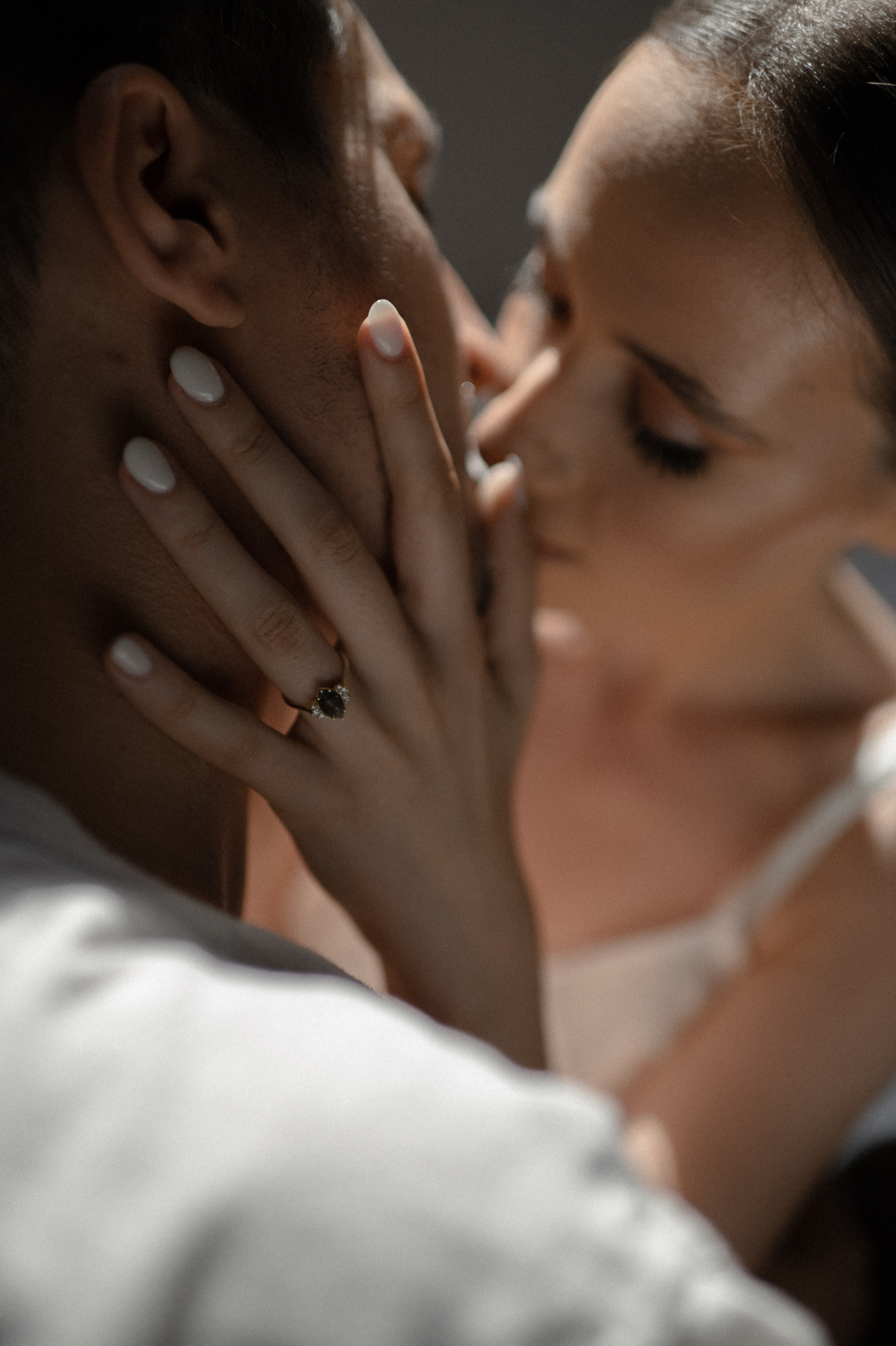 The couple's laughter fills the air as they lovingly kiss, drawing attention to their engagement ring's extraordinary stone, a symbol of their unique bond and commitment to one another.