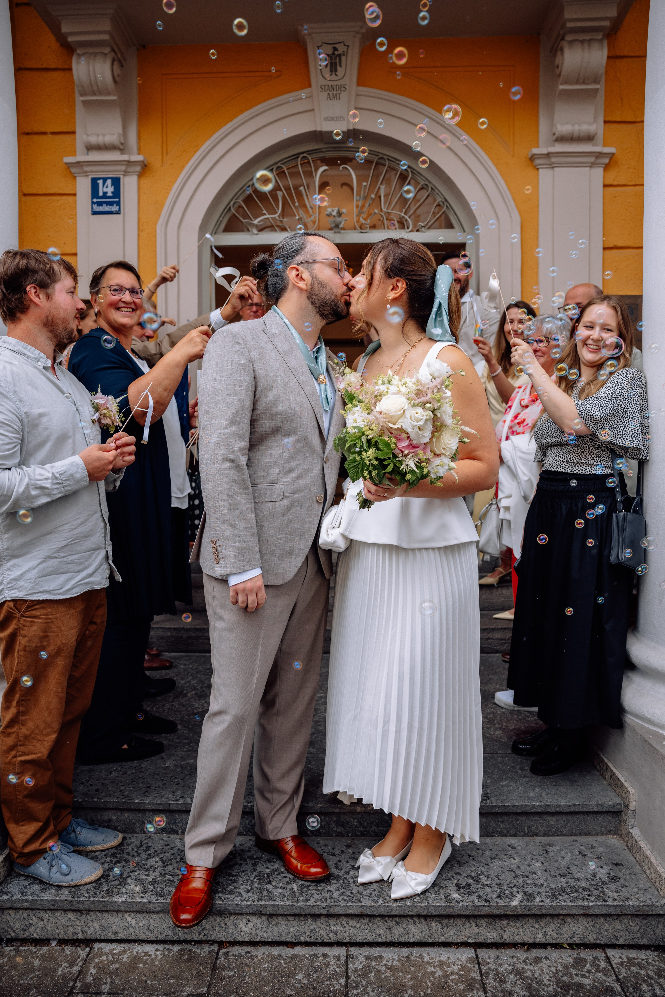 Brautpaar küsst sich vor Standesamt Schwabing – Gäste jubeln und klatschen