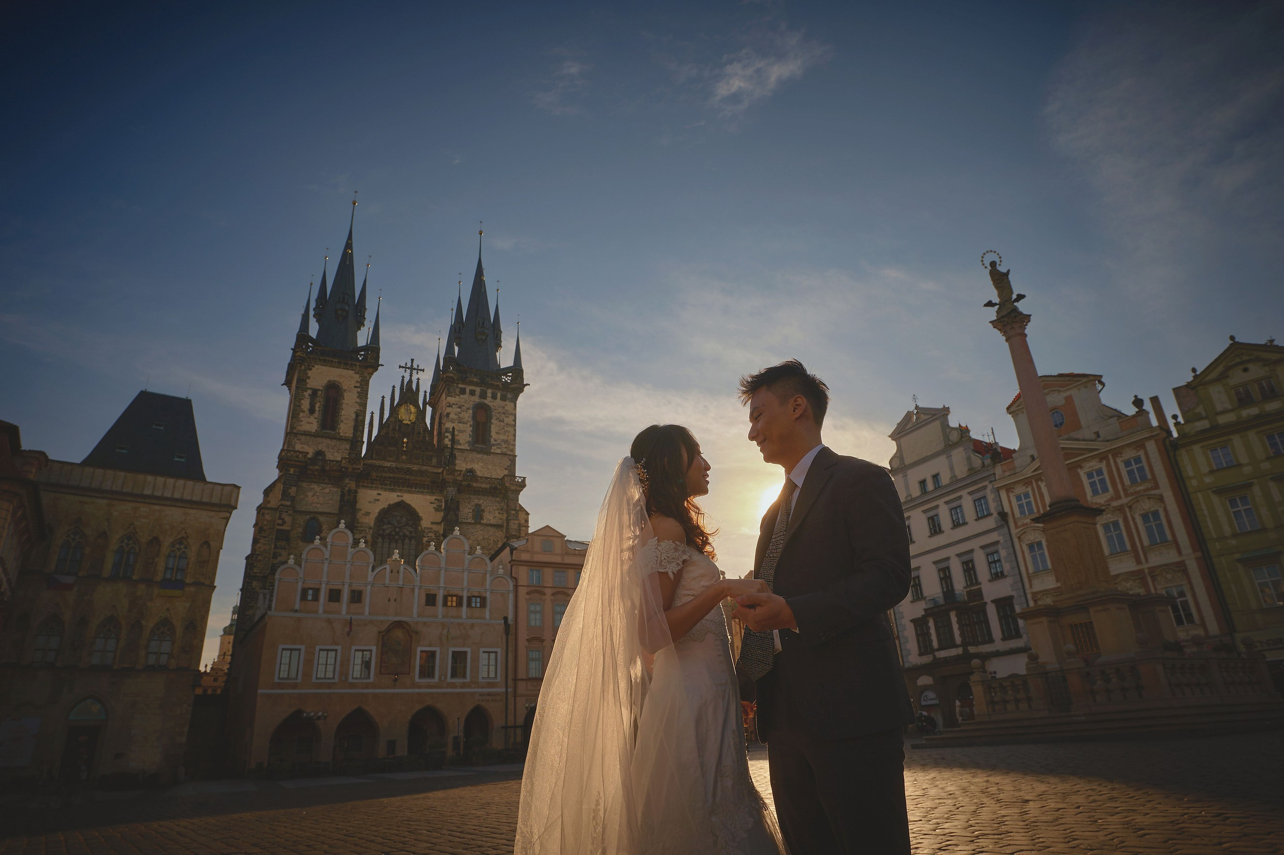 Happy newlyweds Eva and Conan are enjoying a moment in Old Town Square at sunrise.