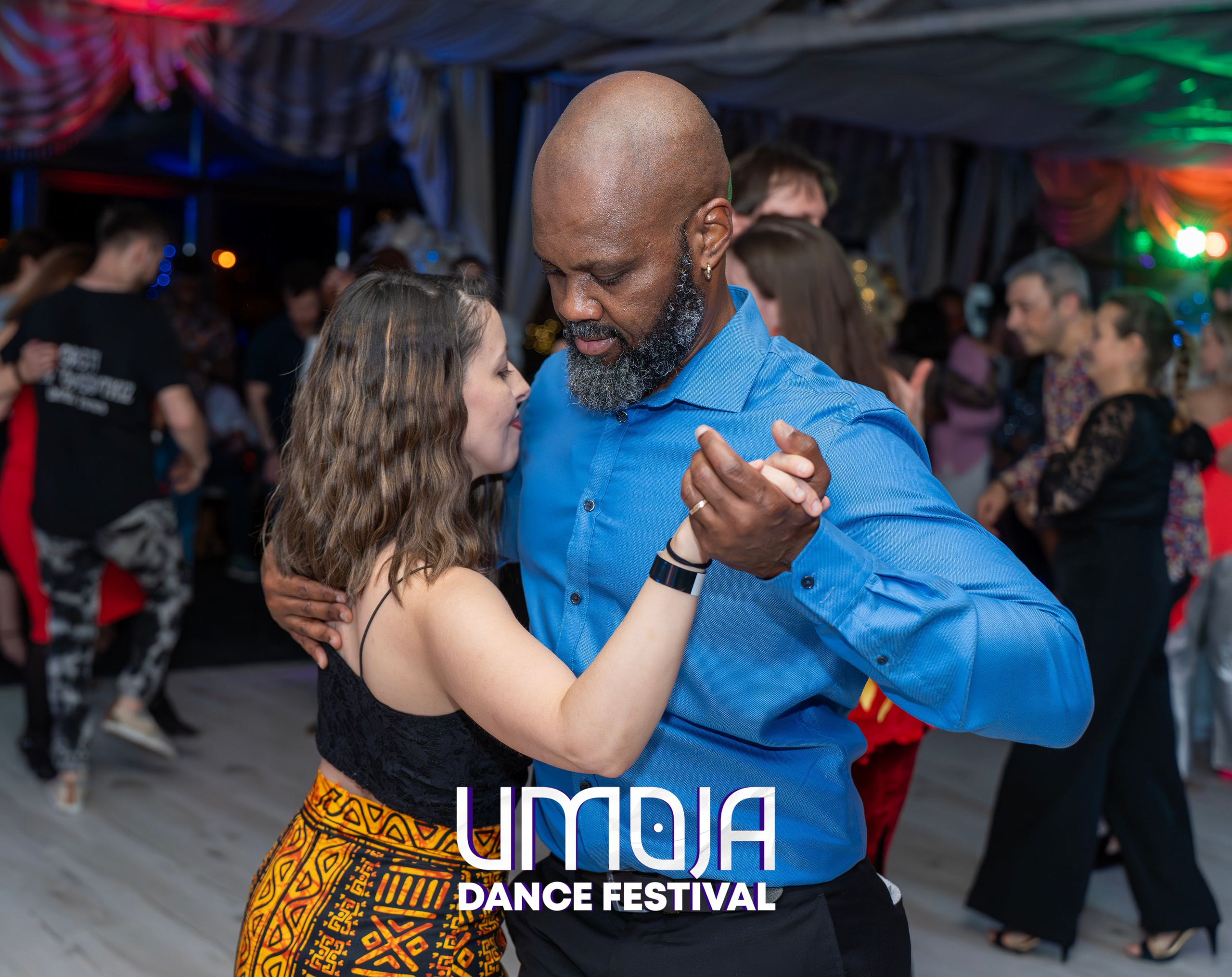 Man and woman dancing closely at an indoor dance festival with other couples in the background.