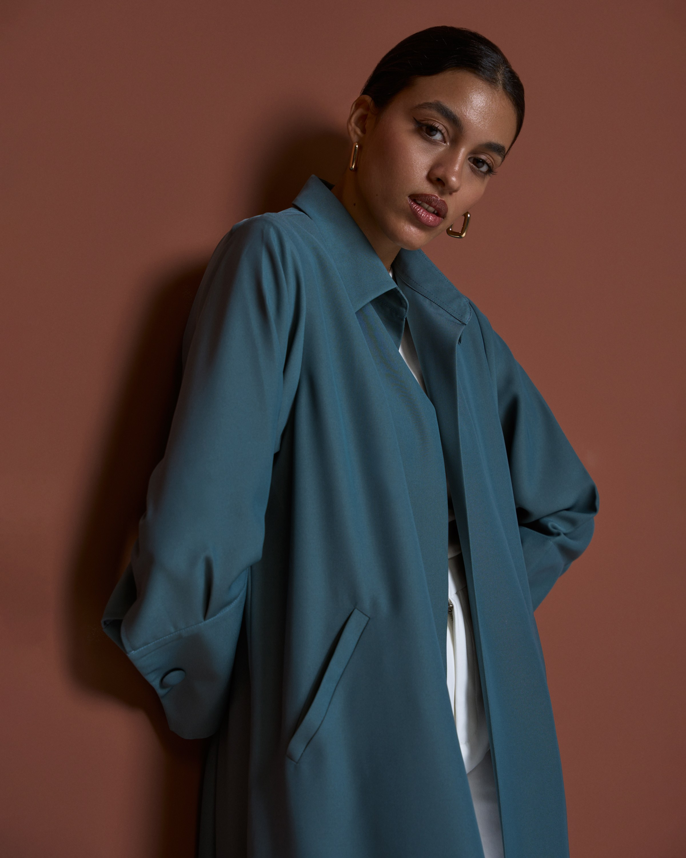 Portrait of a woman wearing a teal coat standing against a brown background