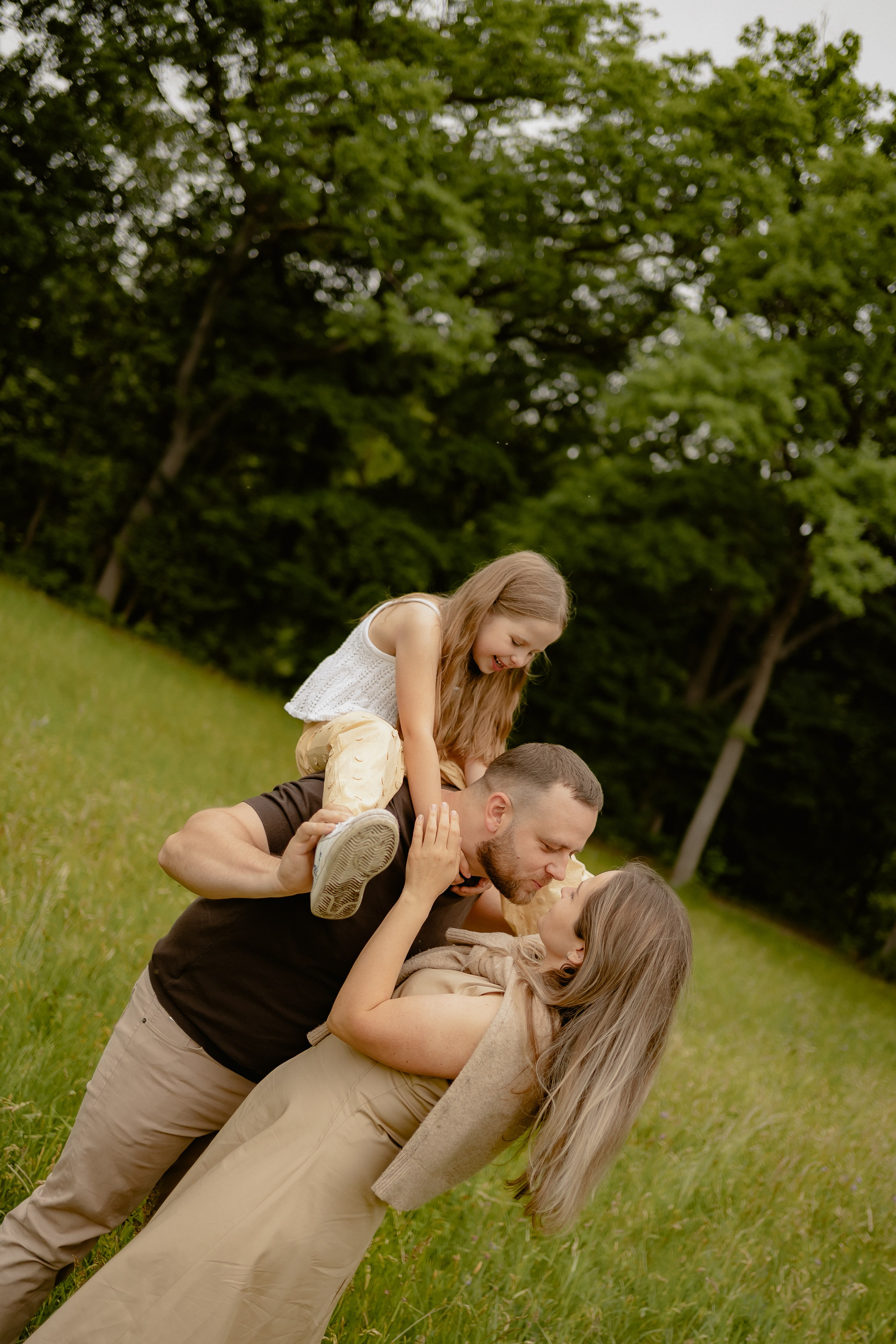 Eltern stehen bei einem entspannten Familienfotoshooting mit ihrer Tochter auf einer Wiese.