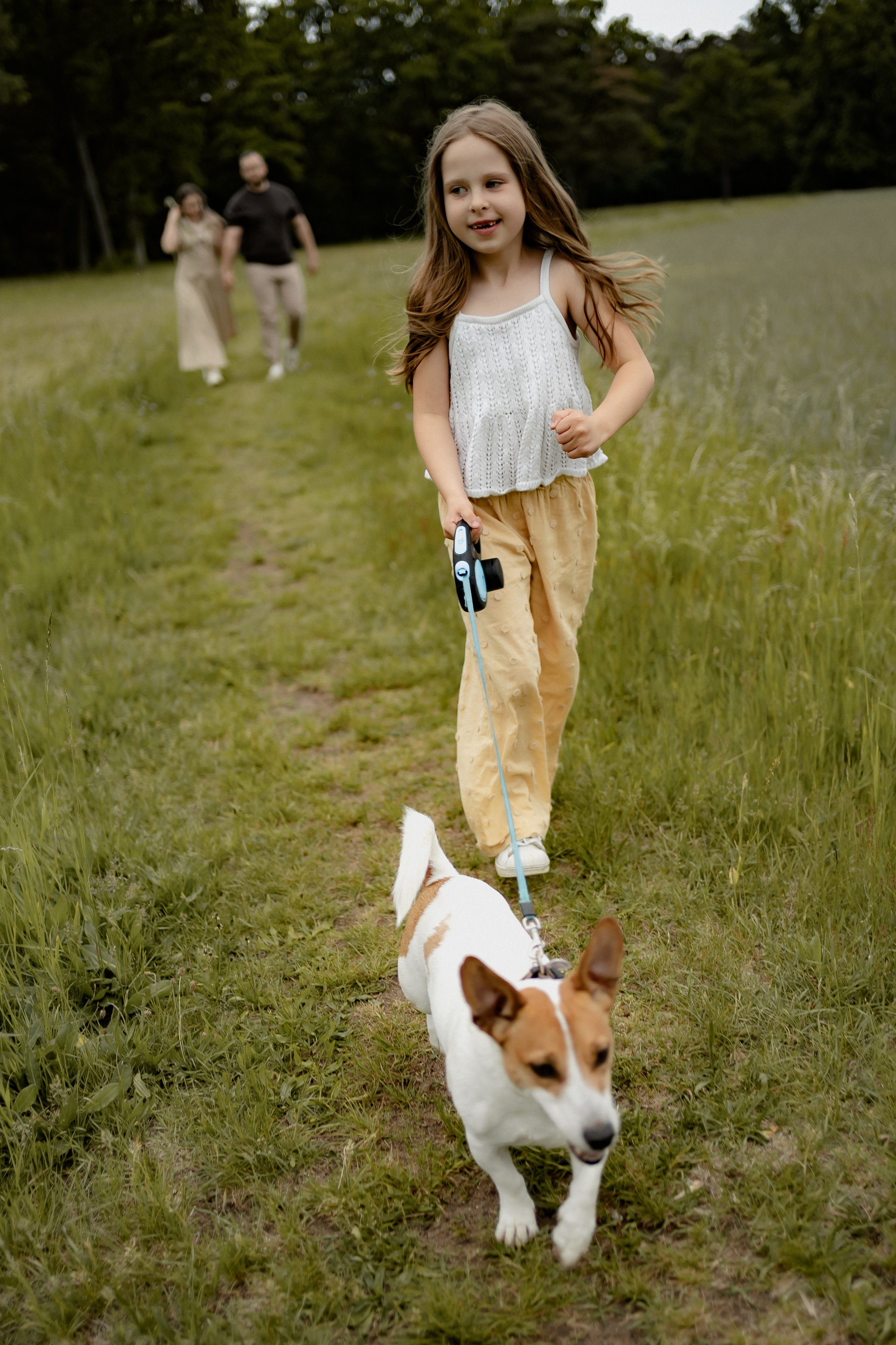 Mädchen spaziert mit dem Familienhund durch eine sommerliche Wiese.